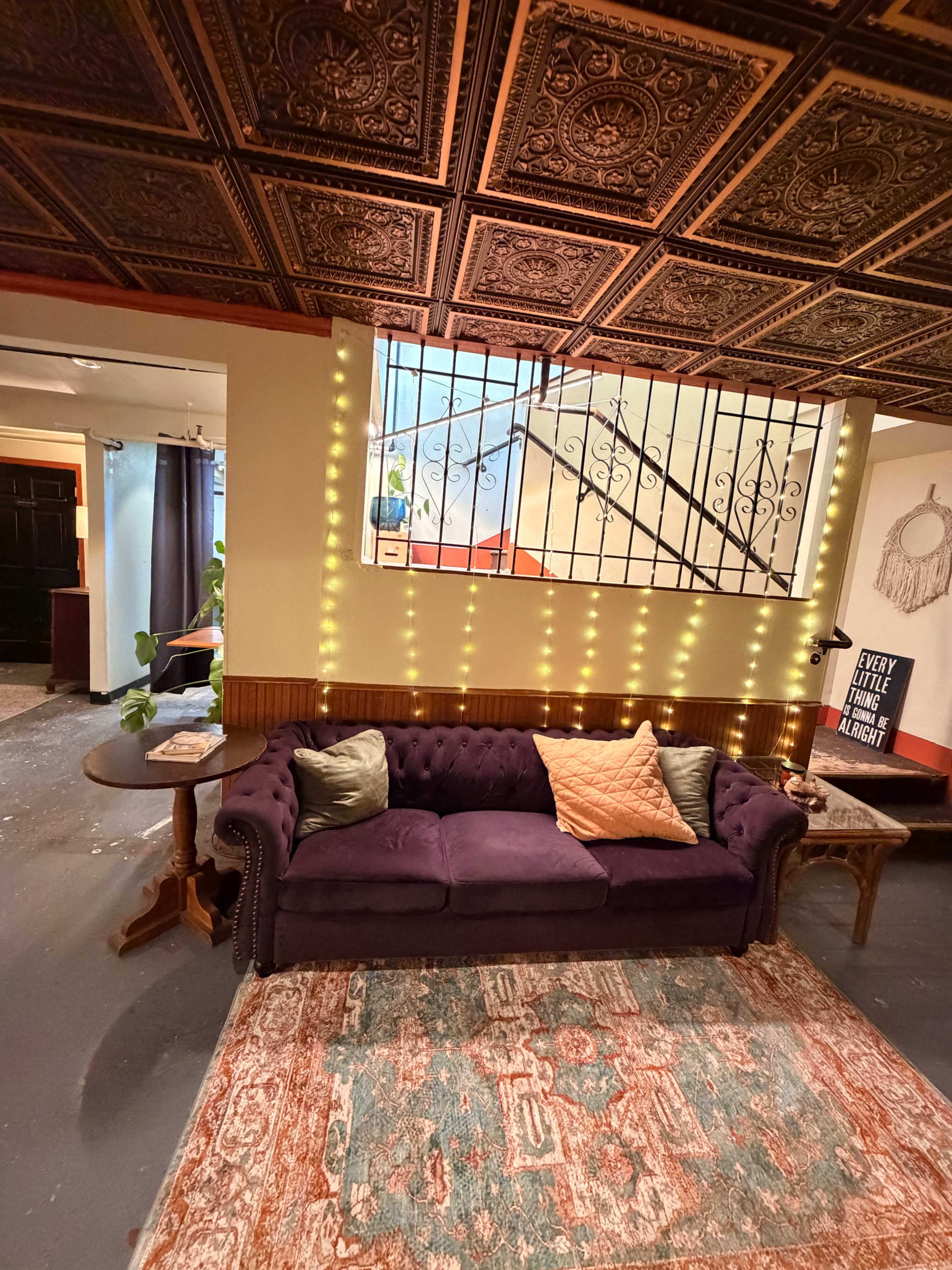 A purple tufted sofa is placed in a room with an ornate ceiling and warm lighting, accompanied by a decorative rug and a small table.
