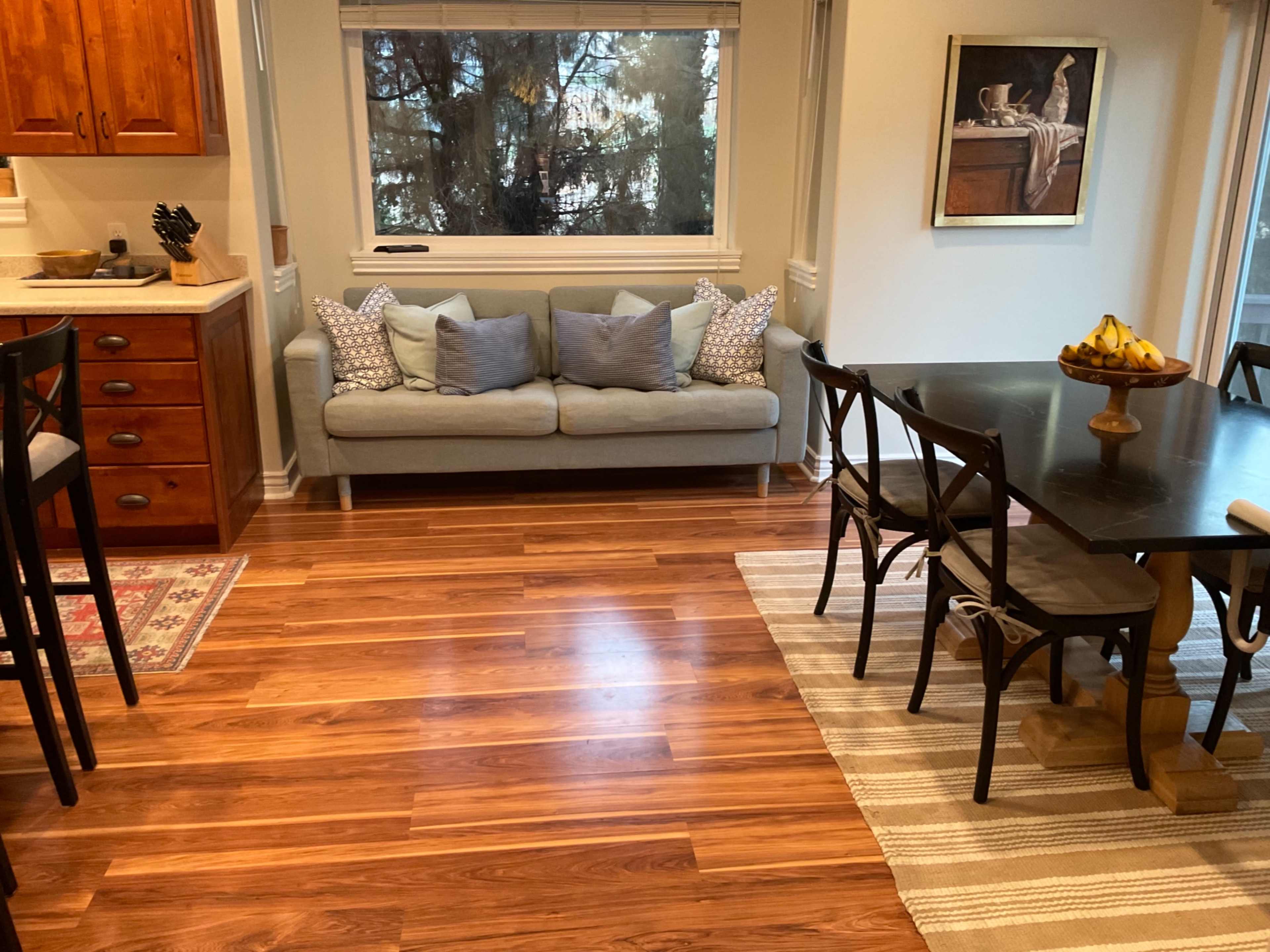 A kitchen area with a small couch and a dining table set against a backdrop of hardwood floors and a window with natural light.