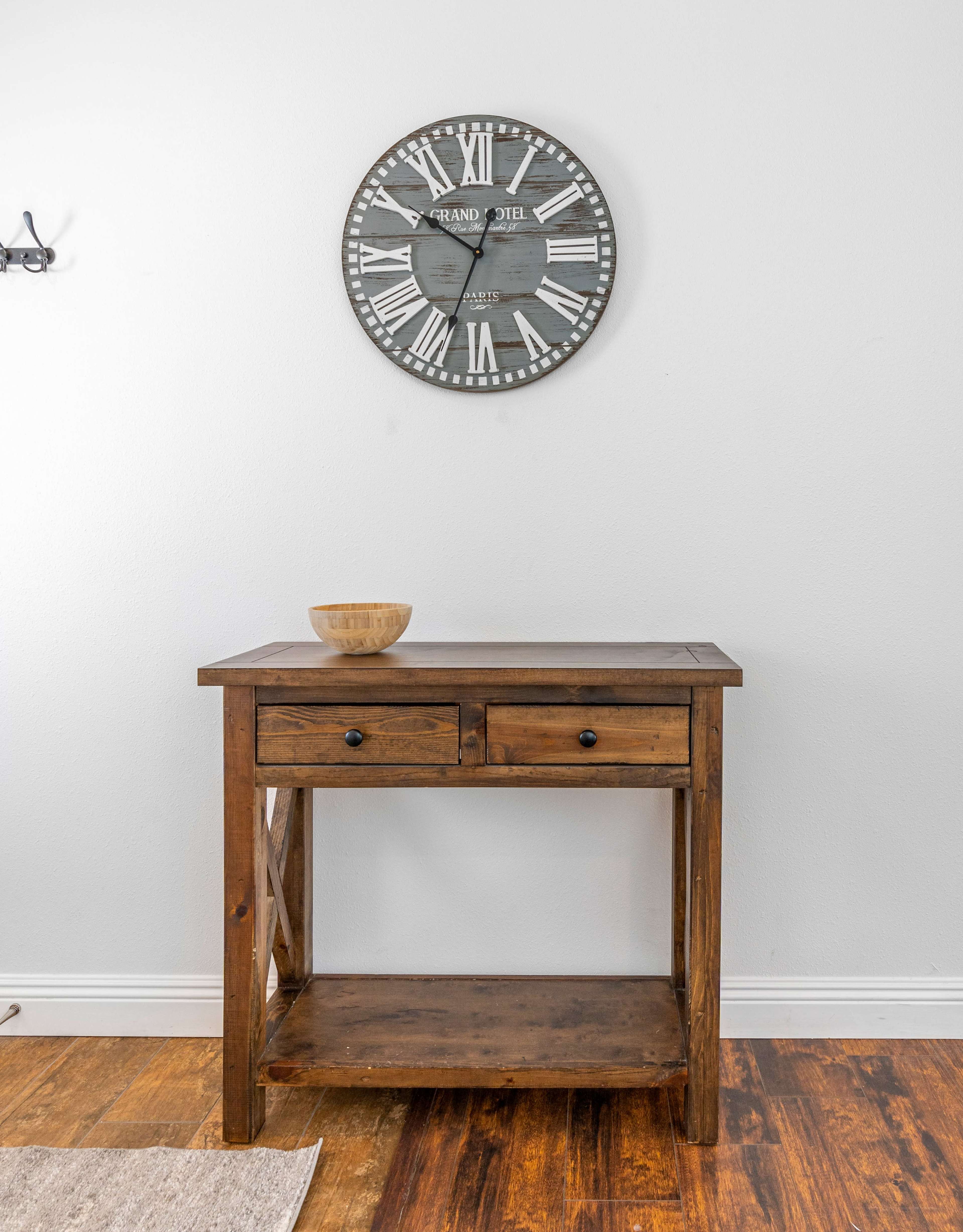 A wooden console table with two drawers and an open shelf is positioned below a large wall clock.