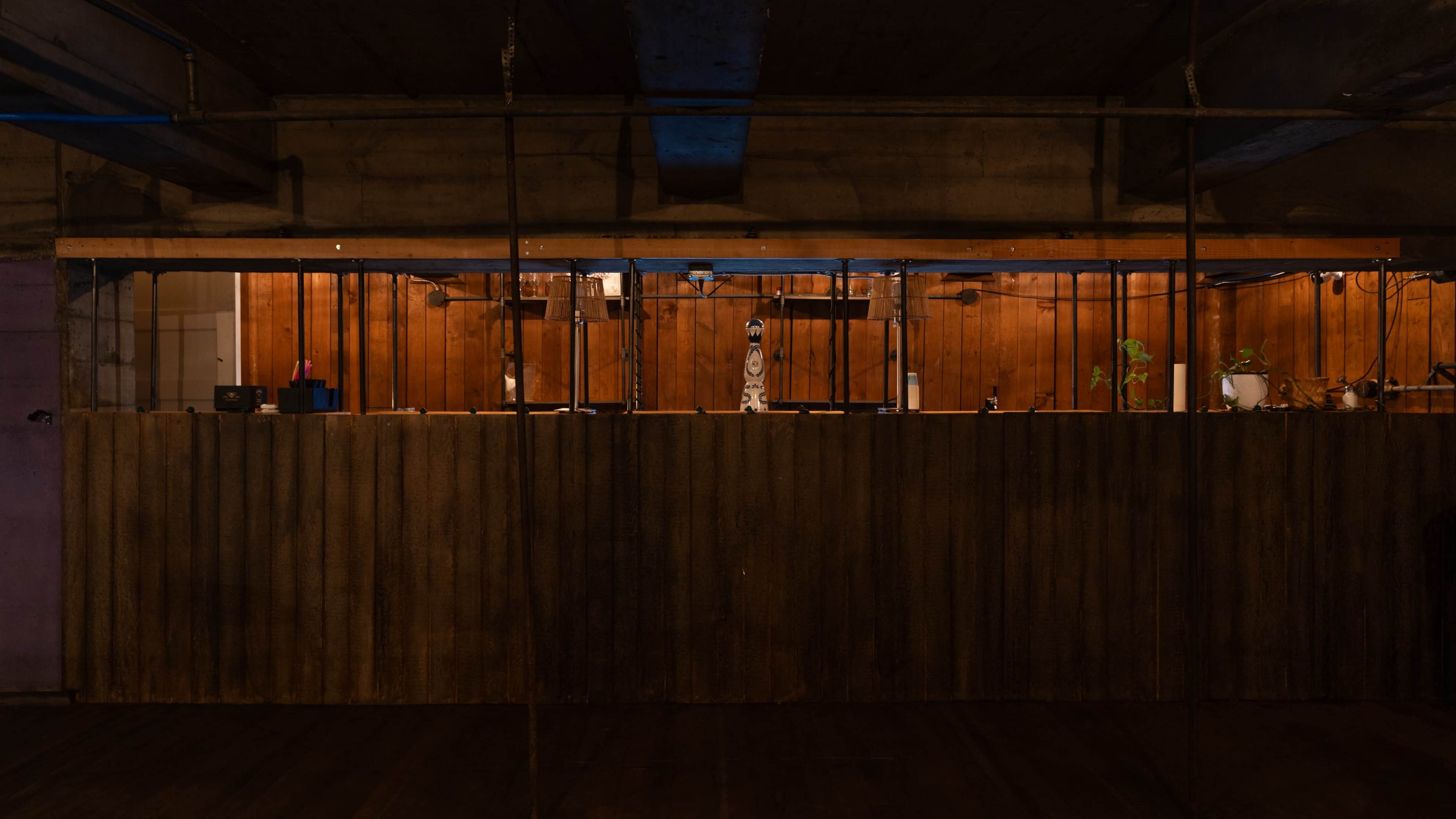 The image shows a dimly lit wooden counter with vertical metal bars in a rustic interior space.