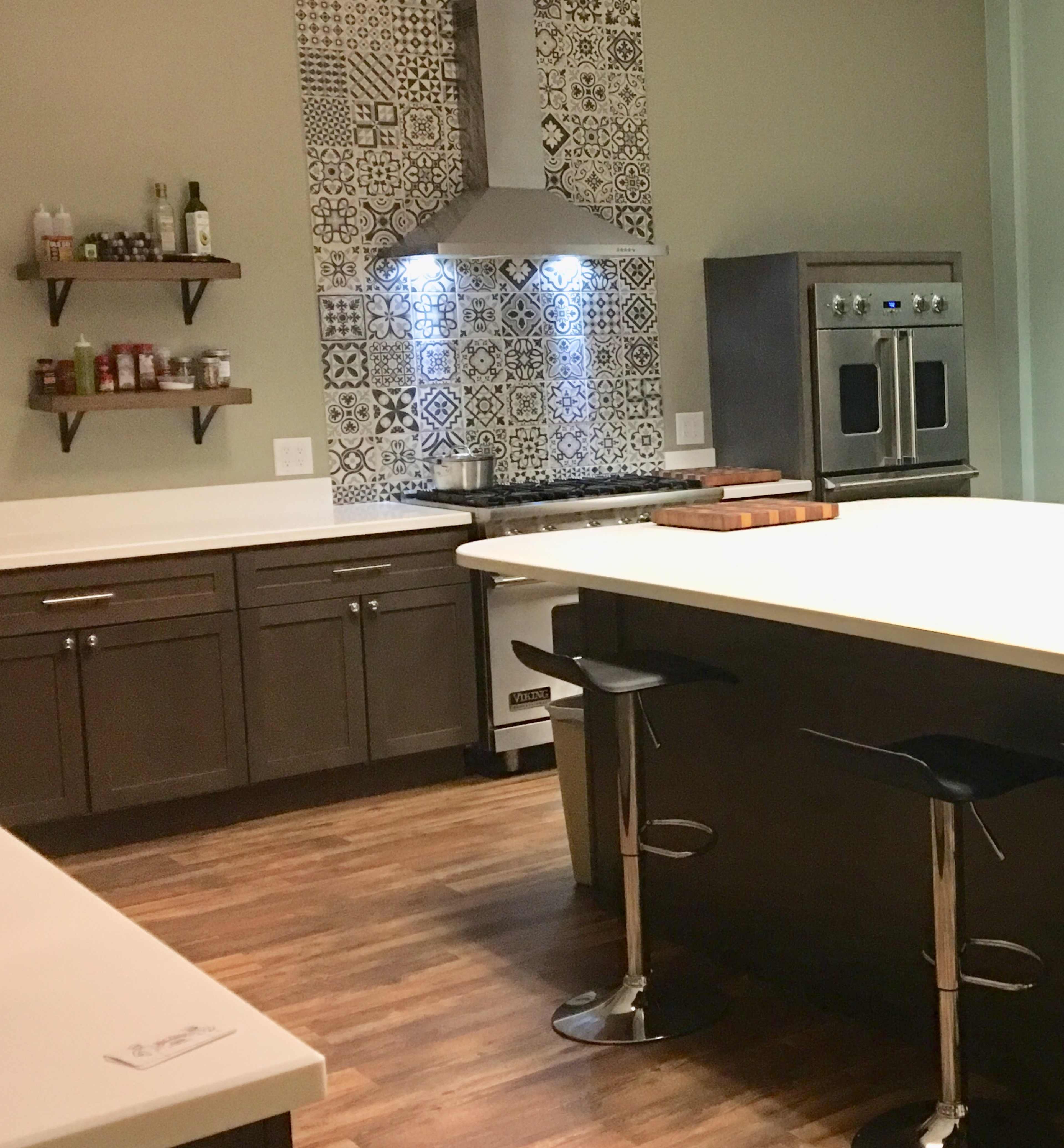 A modern kitchen with a patterned tile backsplash, stainless steel appliances, and a central island with bar stools.