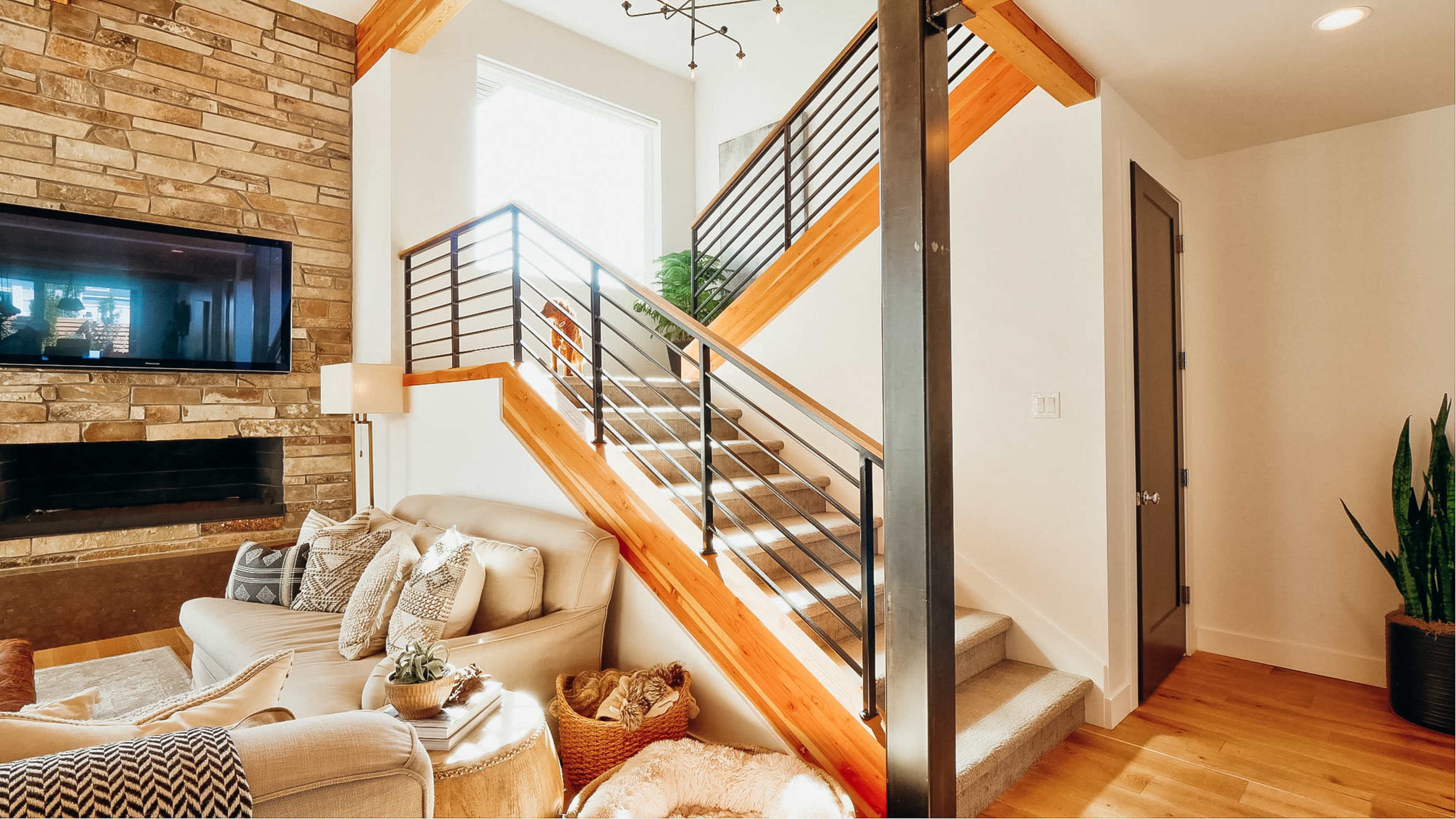 A modern living space with a staircase featuring wooden steps and a metal railing, a stone wall with a television, and a cozy seating area.
