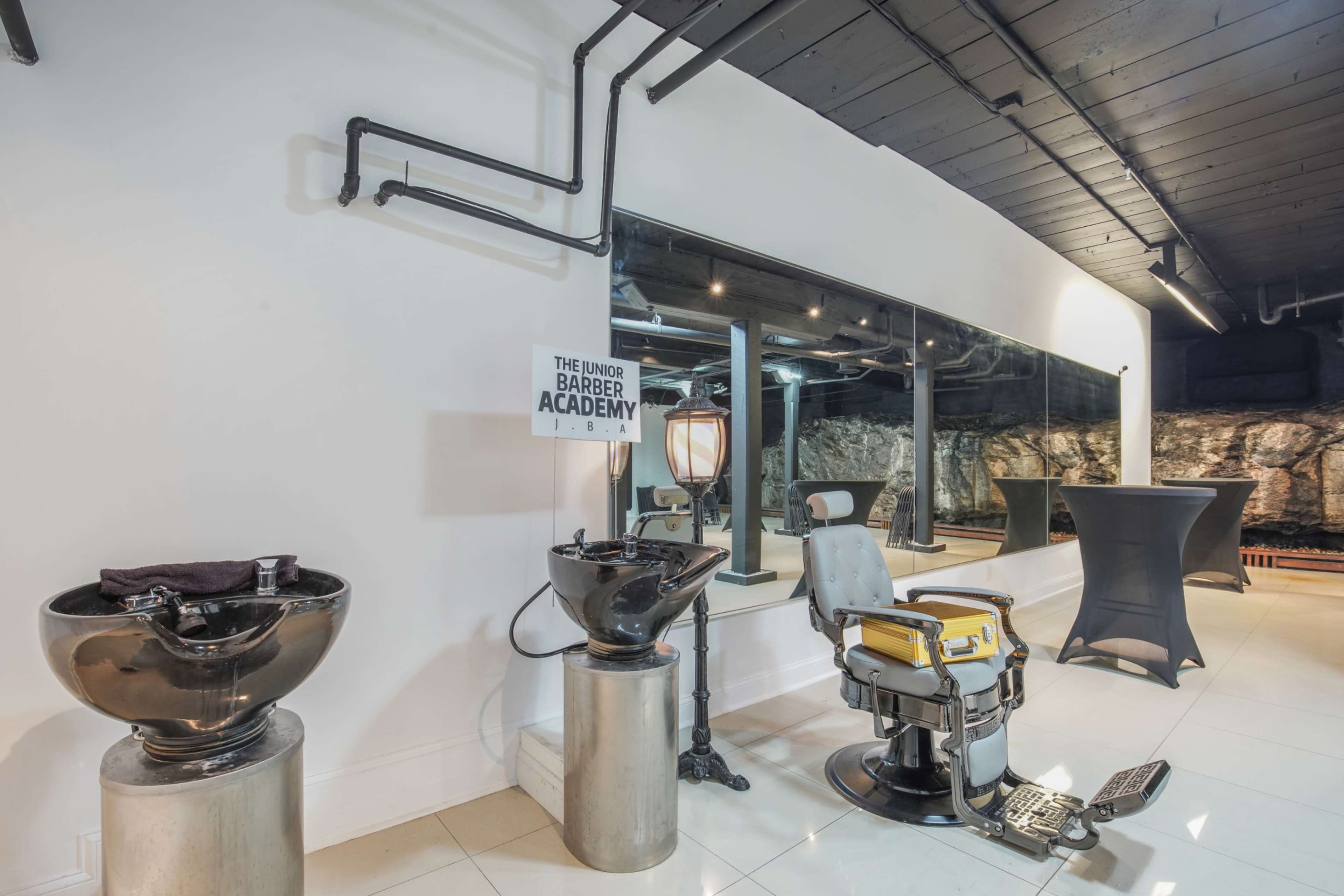 The image shows a modern barber shop interior featuring a barber chair, washbasins, and a wall-mounted sign for "The Under Barber Academy."