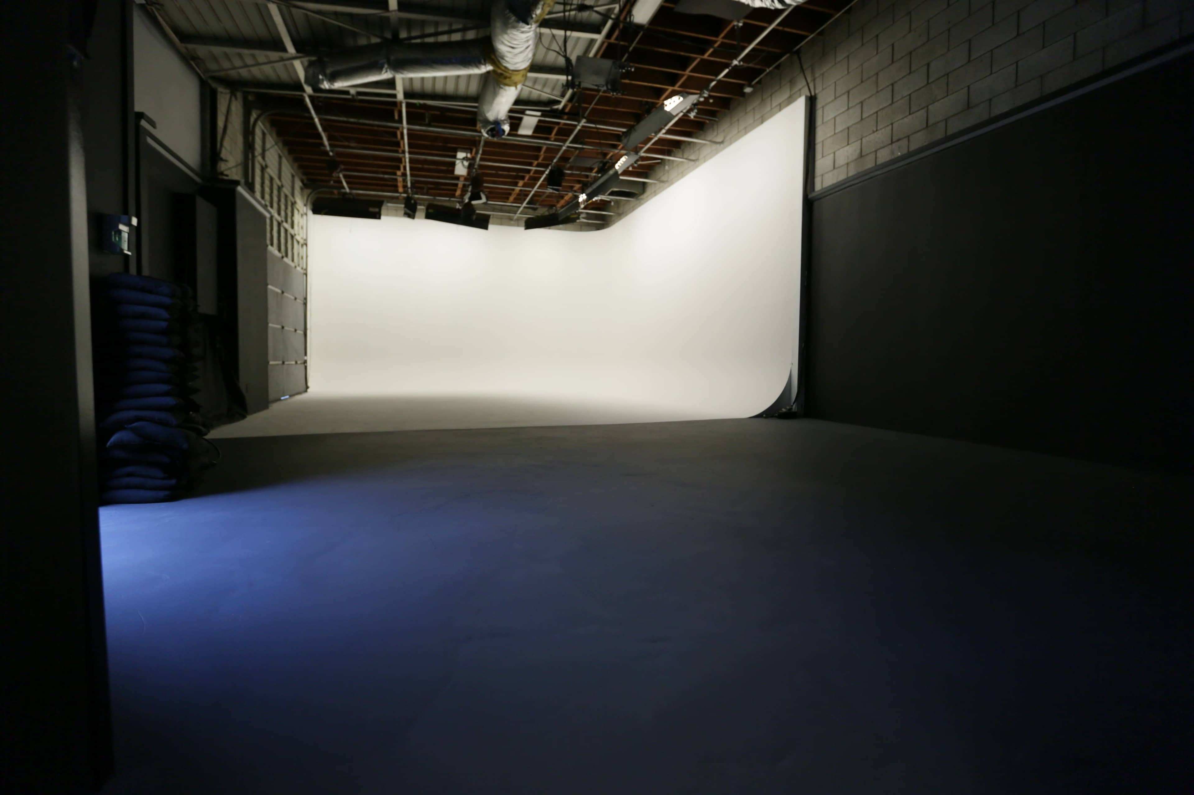 The image shows a spacious photography studio with a seamless white backdrop and dark flooring.