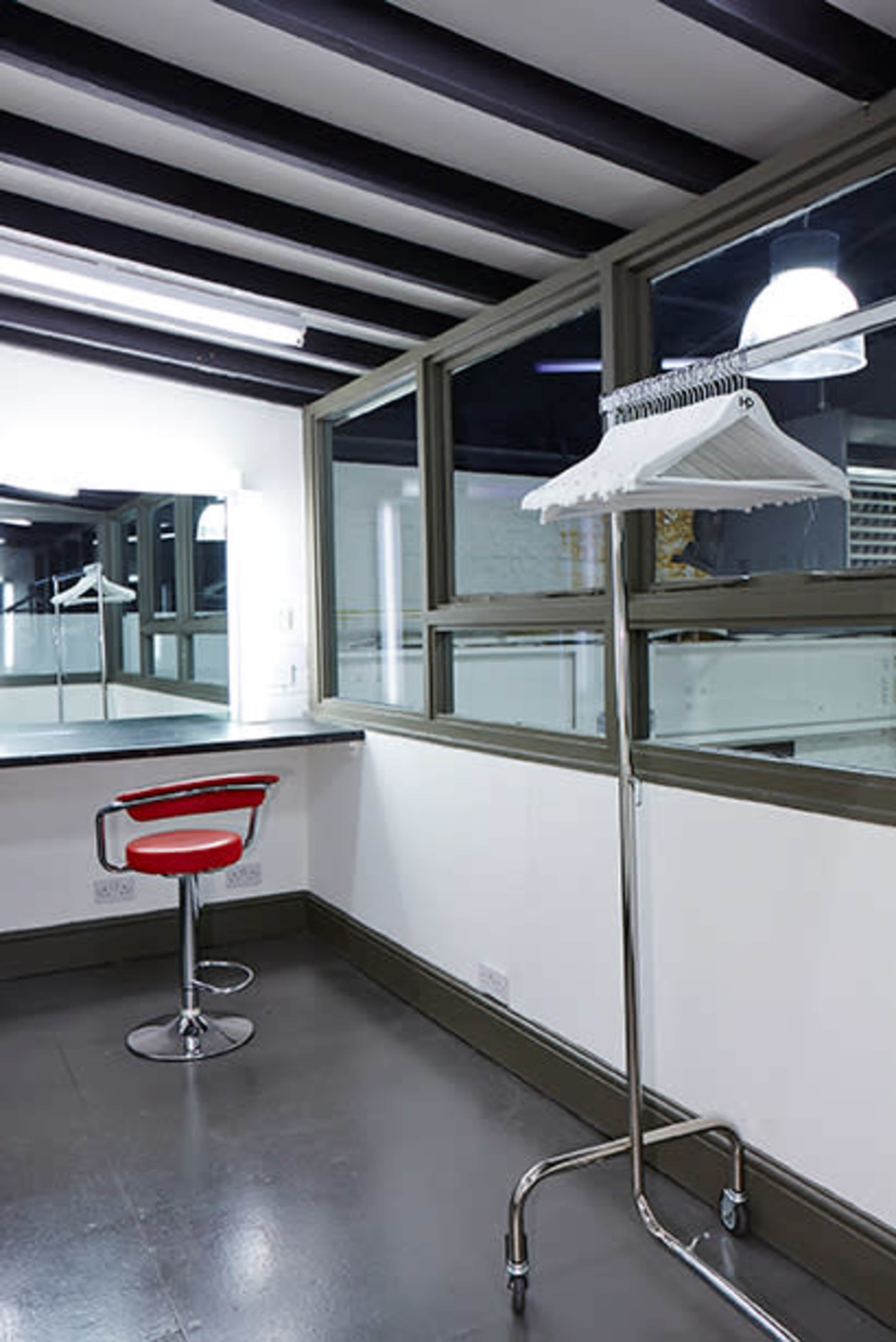 A modern room with a red swivel chair and a clothes rack, featuring large windows and a mirror.
