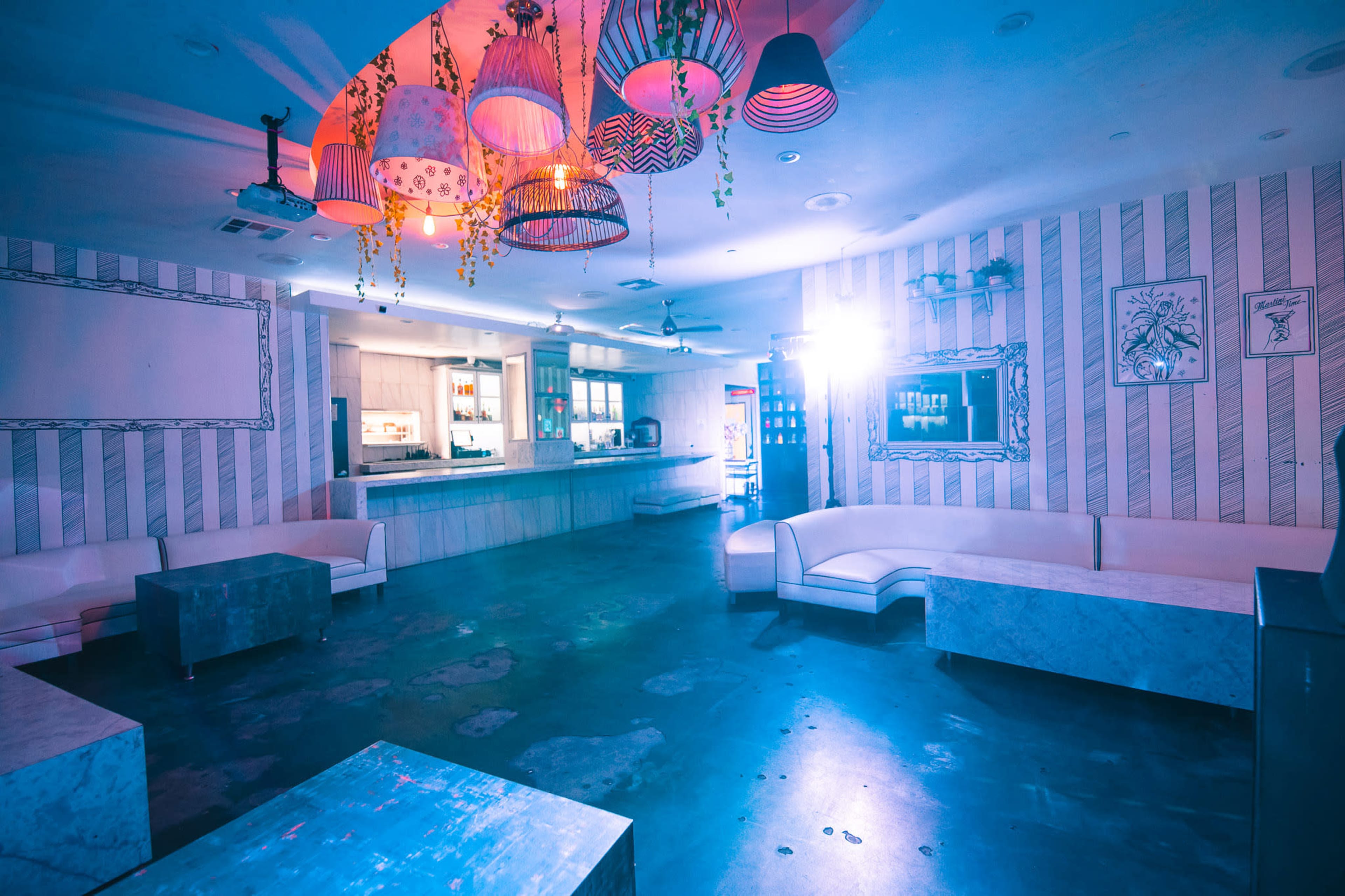 The image shows a spacious indoor venue with striped walls, round lights hanging from the ceiling, and minimalist furniture arranged around the room.