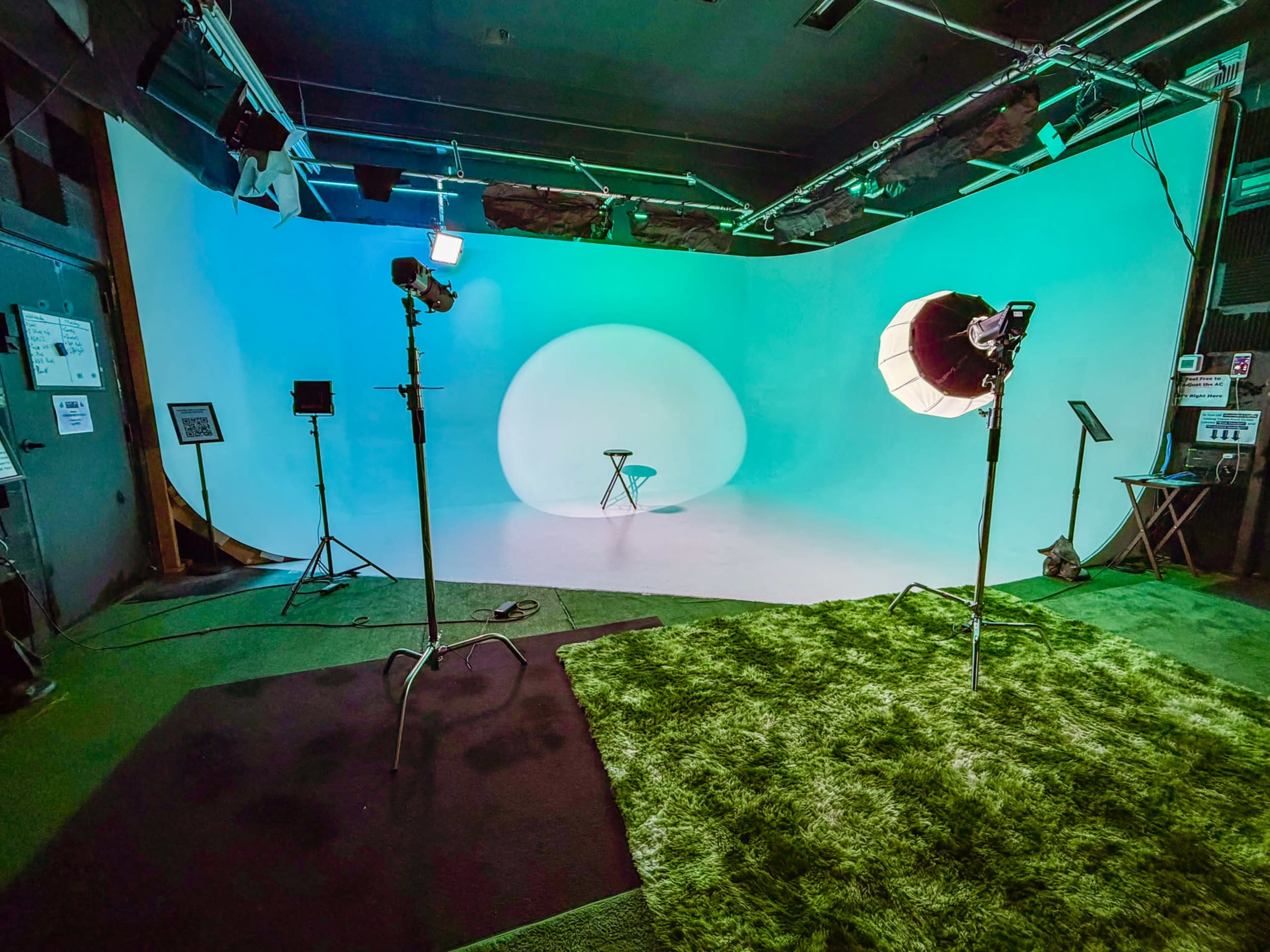 The image shows a photography studio with a circular backdrop, lighting equipment, and a stool in the center of the scene.