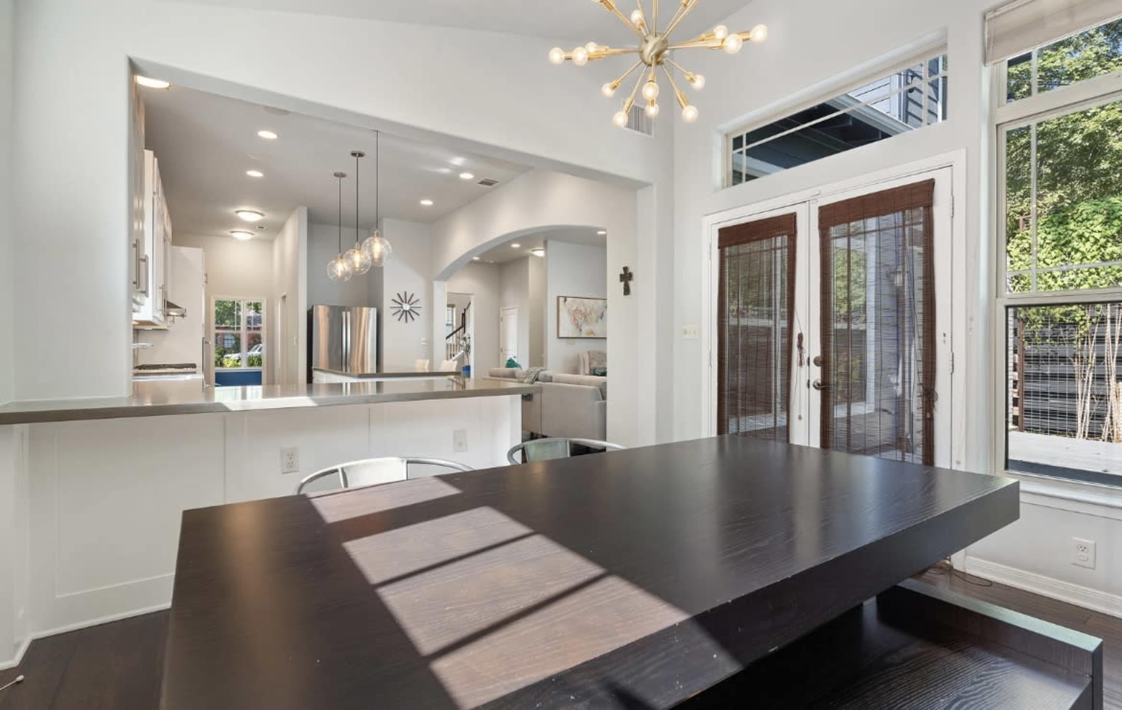 The image shows a modern dining area with a dark table, large windows, and a light fixture hanging above.
