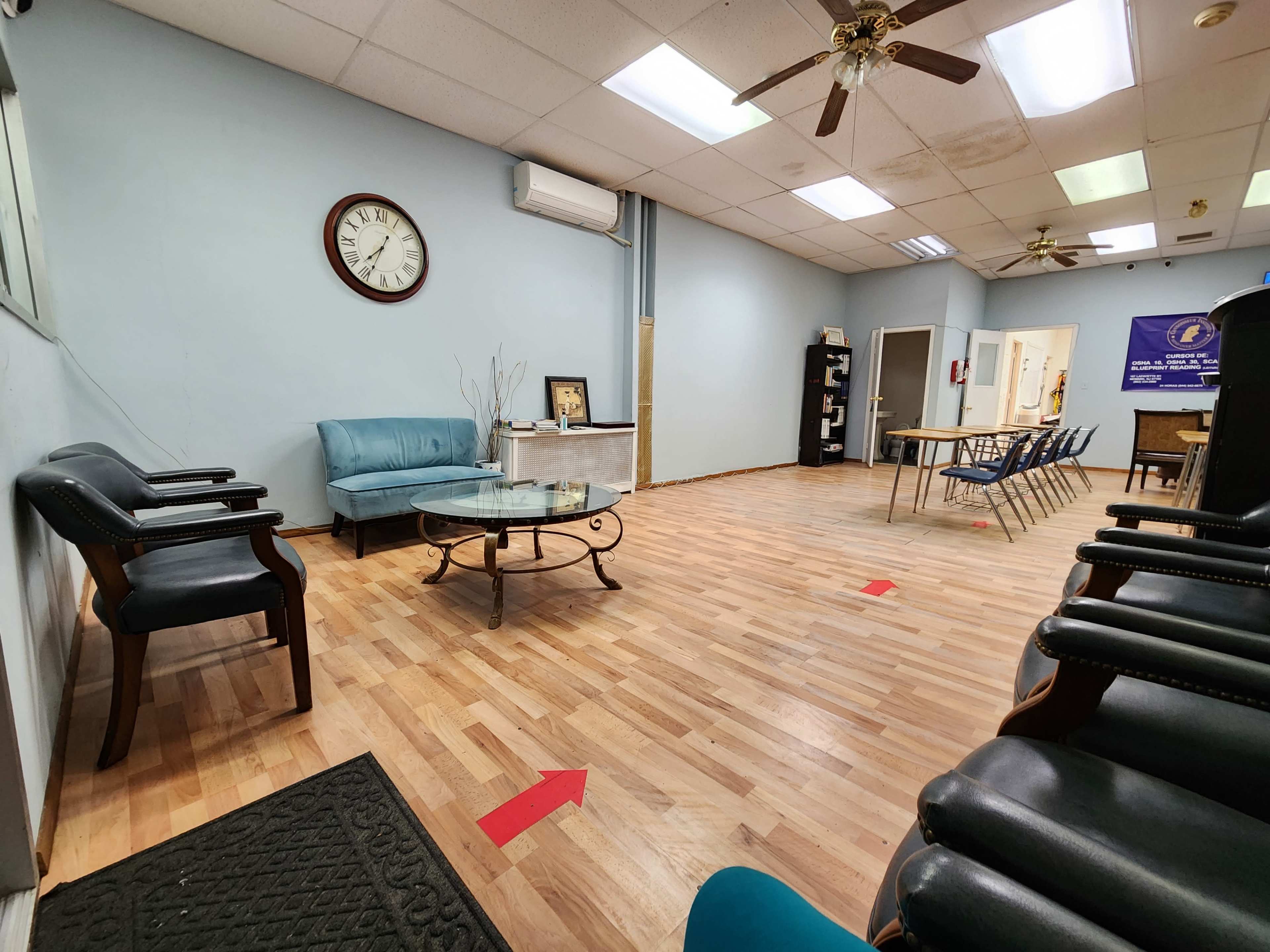 A spacious waiting room features a blue couch, a glass coffee table, and several chairs arranged around a wooden floor.