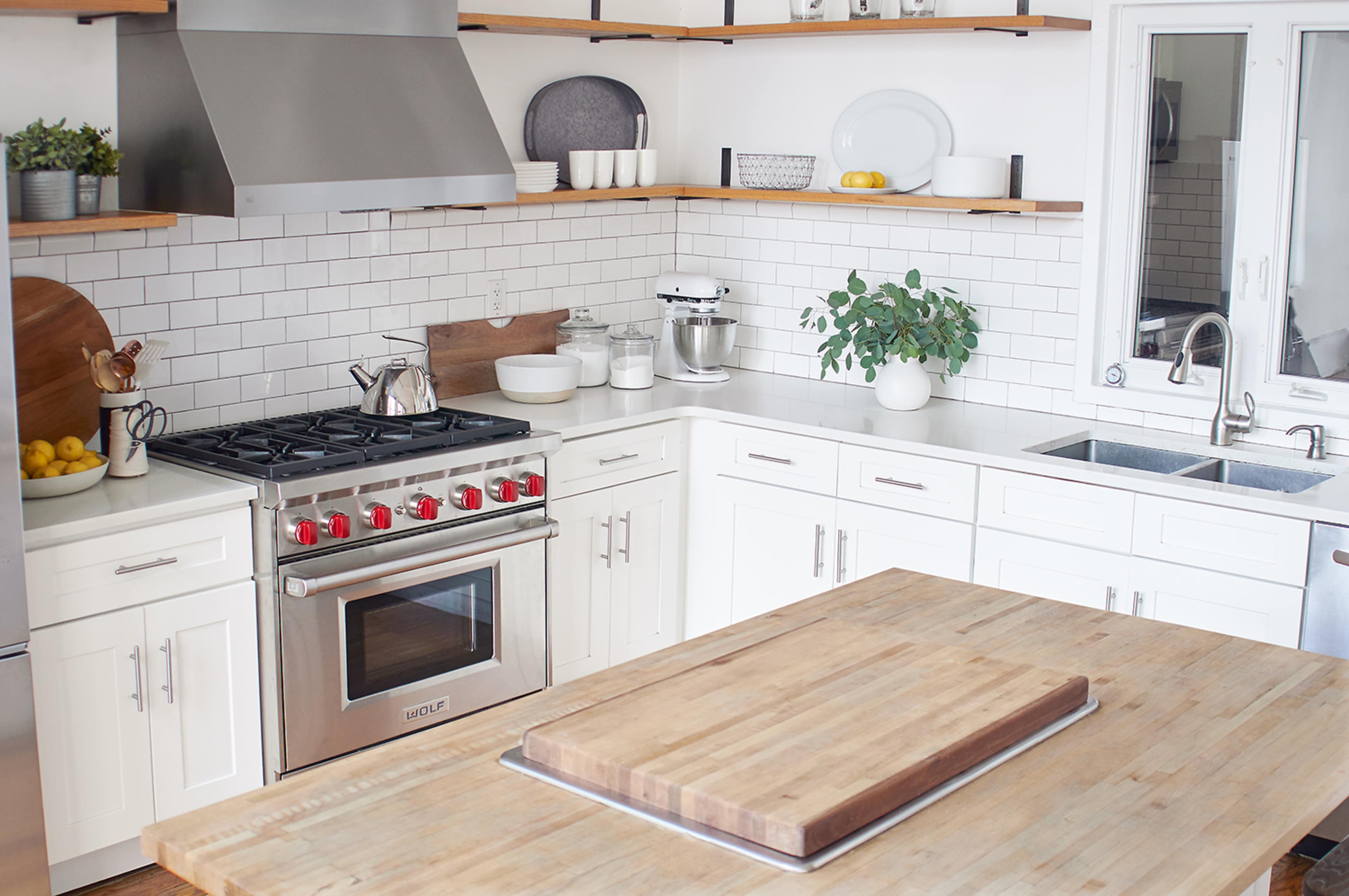 The image shows a modern kitchen with stainless steel appliances, white cabinetry, and a large wooden island in the center.