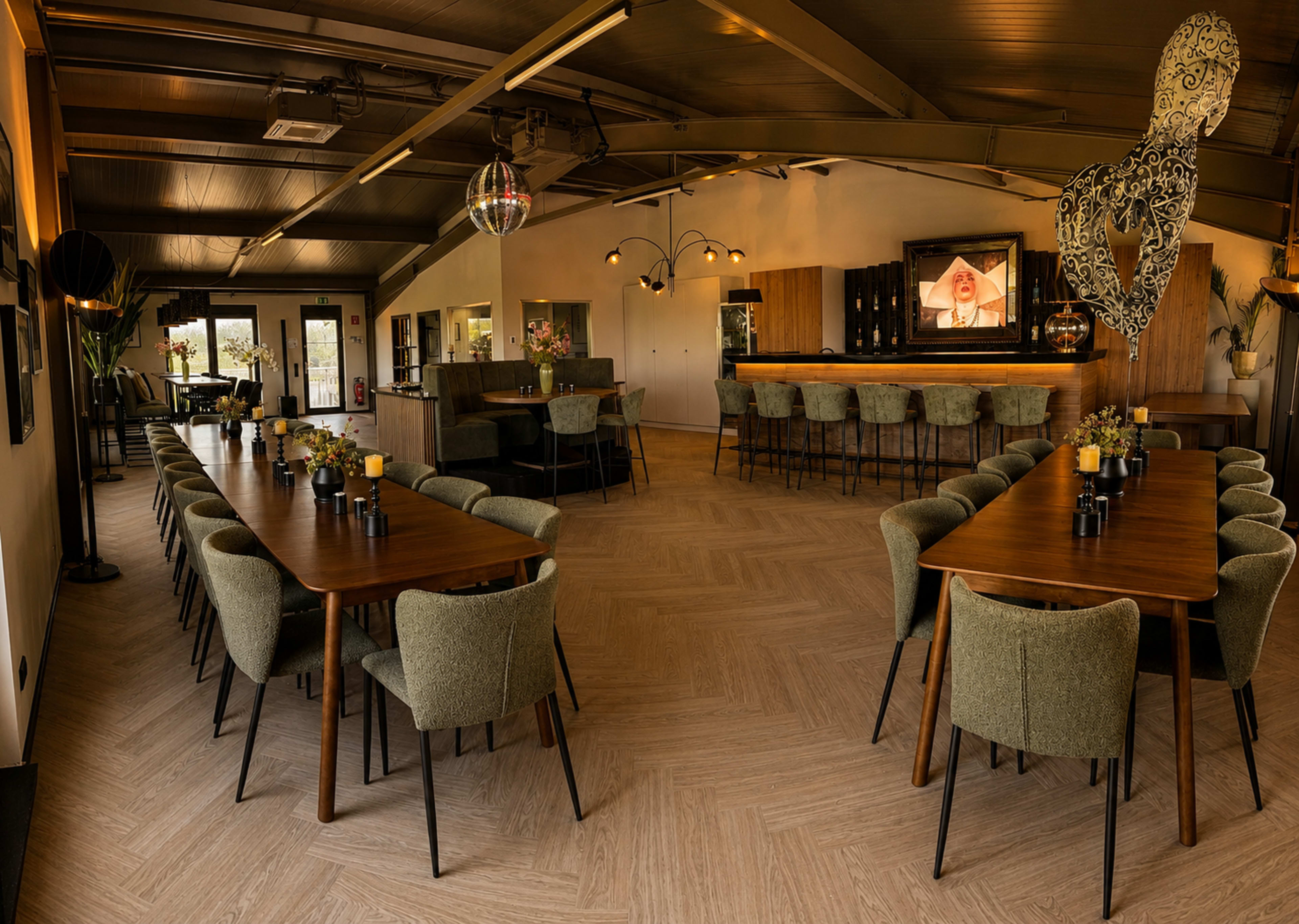 The image shows a spacious dining area with multiple wooden tables, green upholstered chairs, decorative lighting, and a bar area in the background.