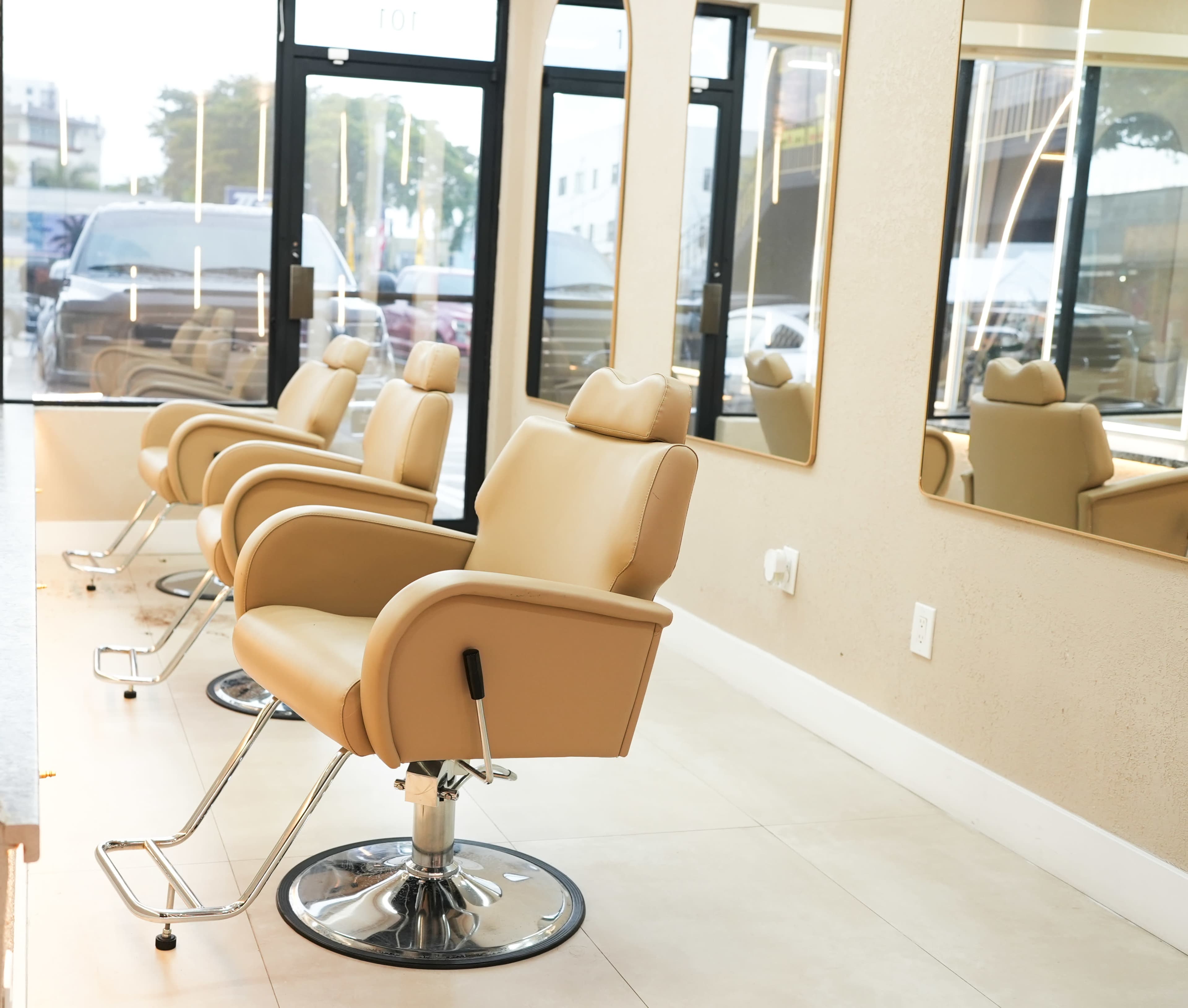 The image shows several empty salon chairs arranged in a modern hair salon with large mirrors and a bright, open atmosphere.