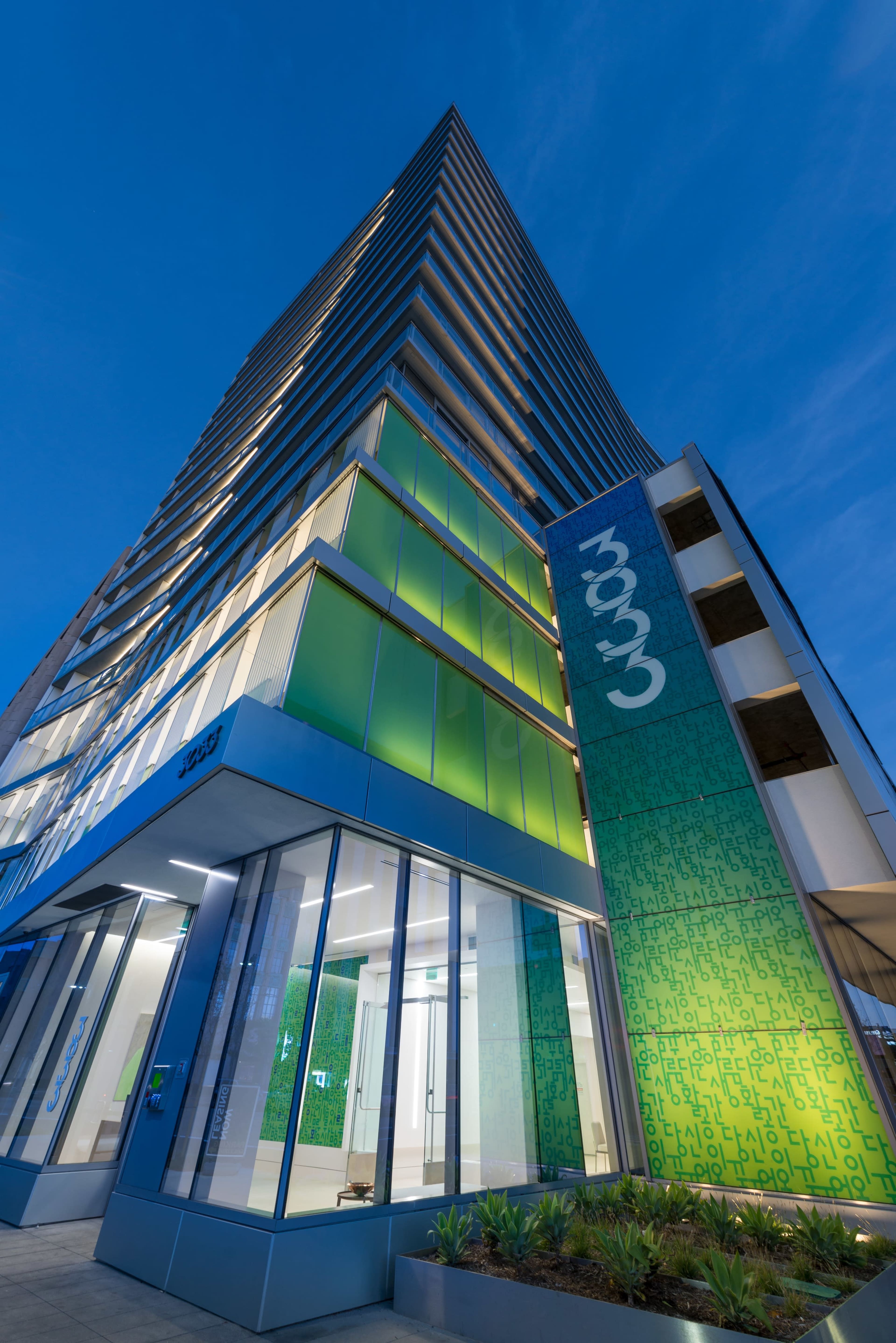 A modern green and glass building reaches Skyward, featuring prominent signage on its façade.