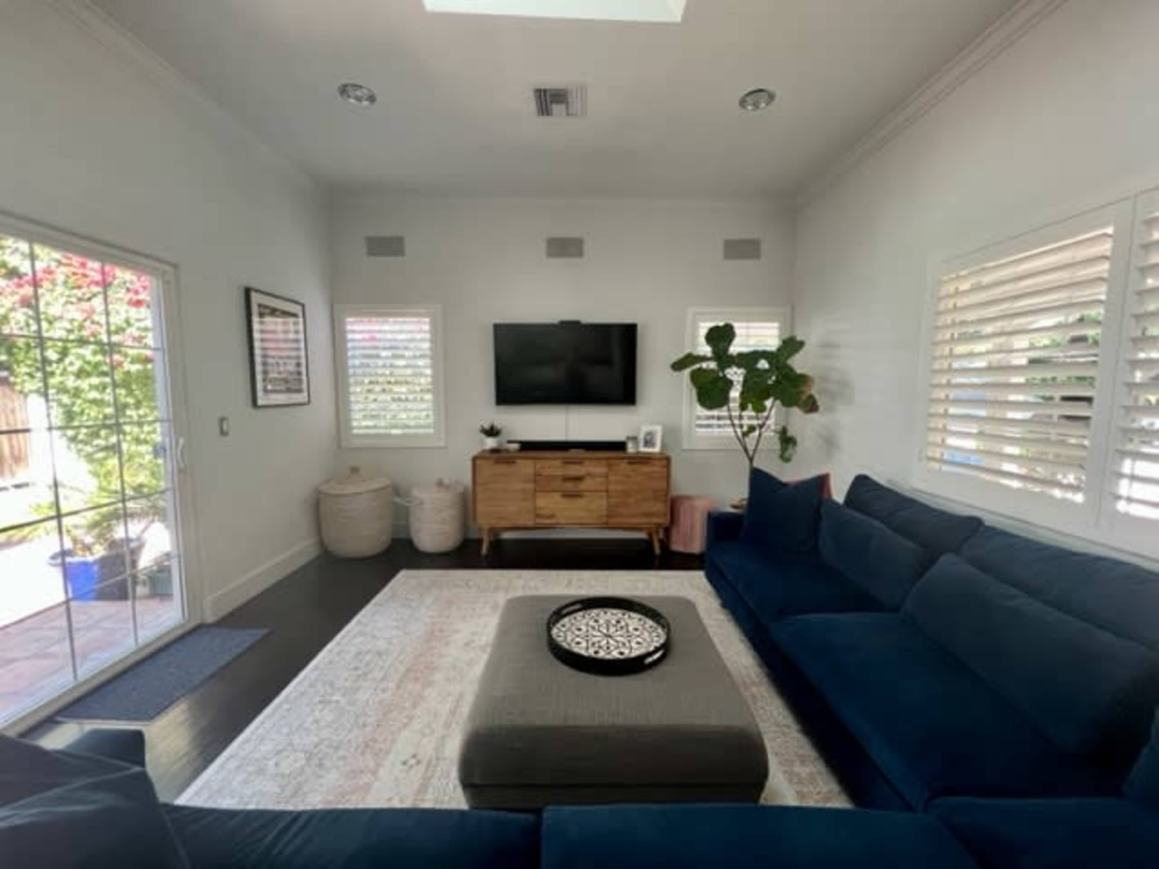 The living room features a blue sectional sofa, a wooden television stand, and a large window with plantation shutters.