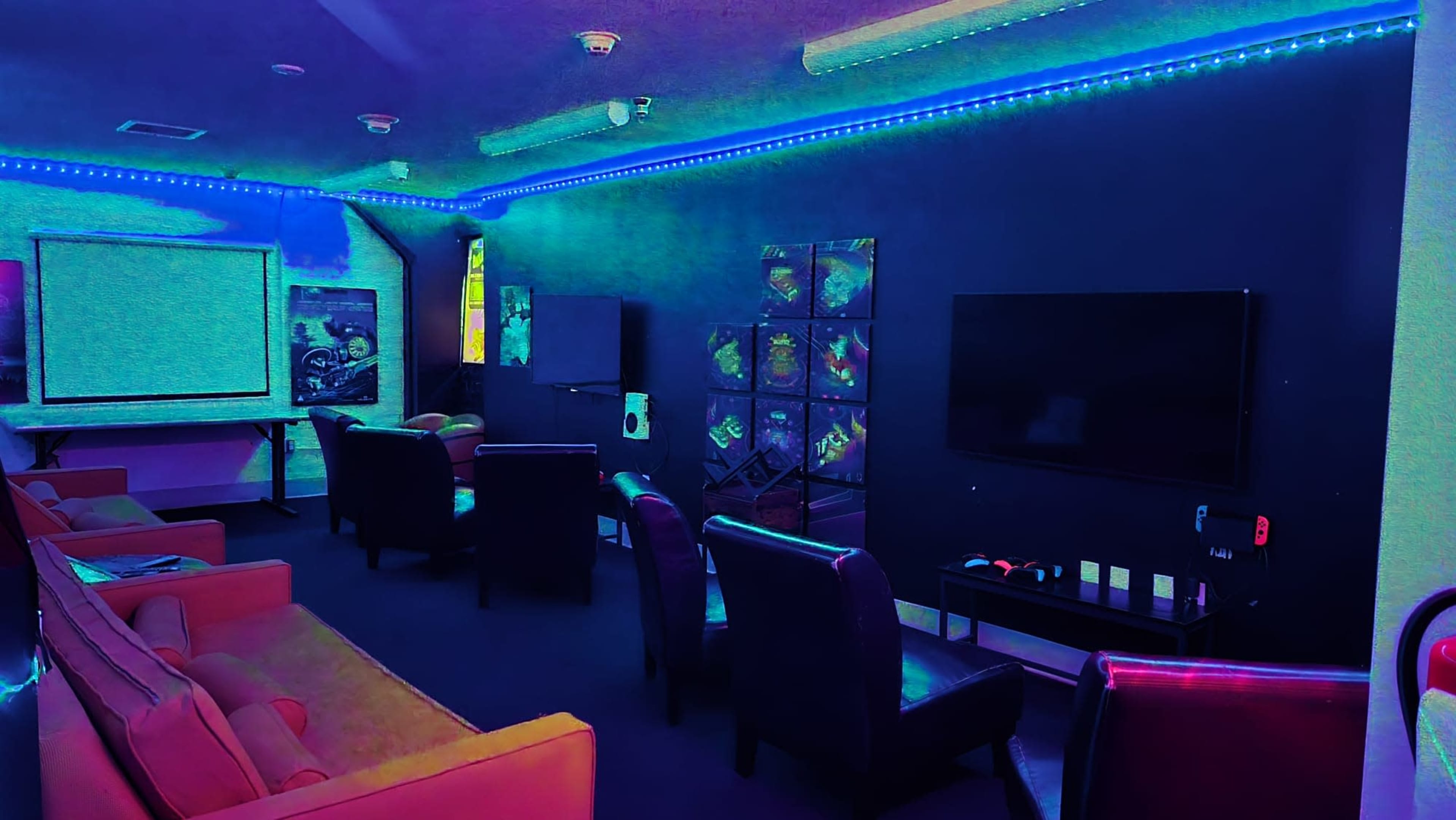 The room features several seating areas with dark walls illuminated by neon lights and displays, including a large screen and several framed artworks.