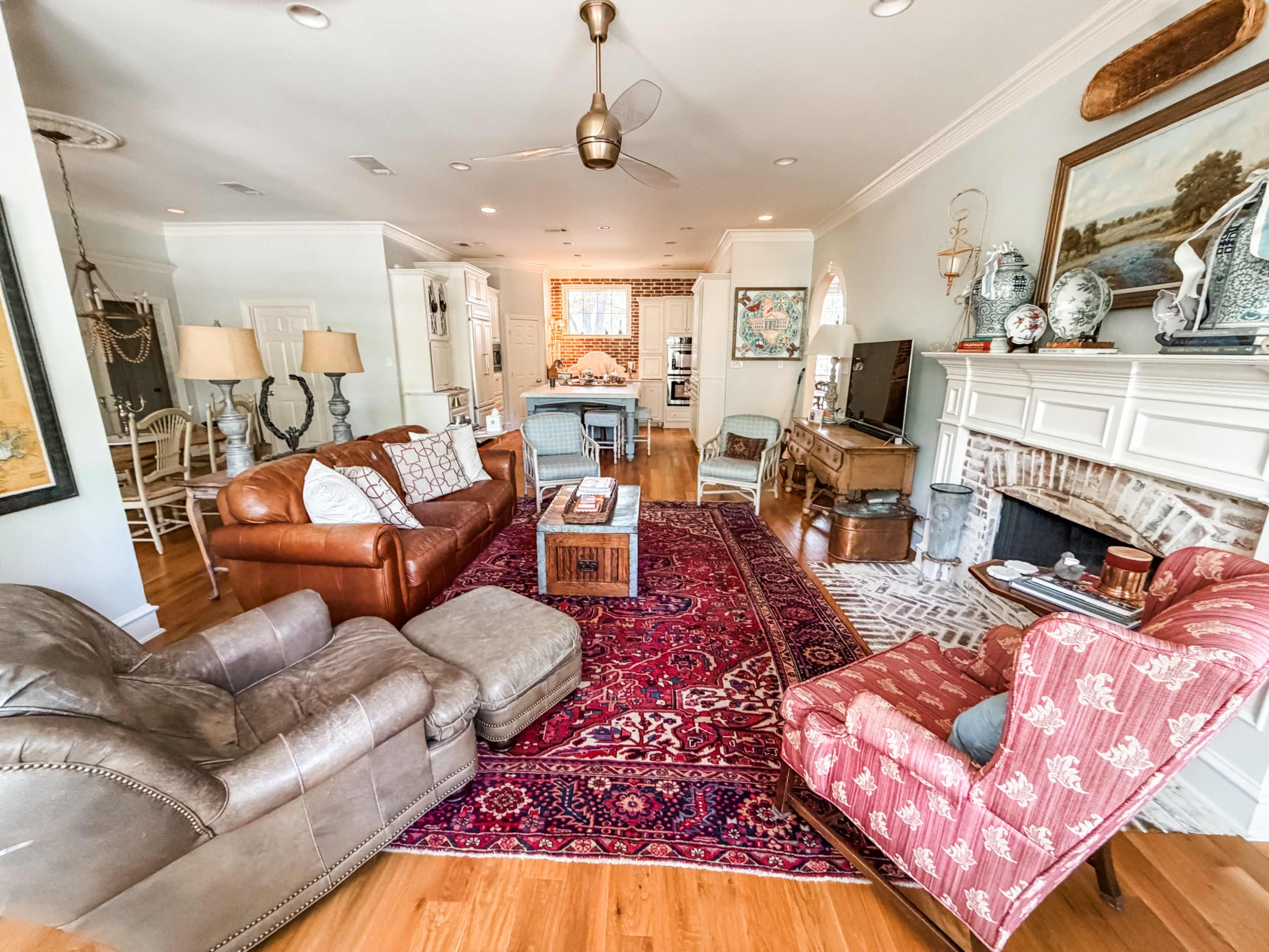 The image shows a cozy living room with a leather sofa, armchairs, a coffee table, and a fireplace, all arranged around a large area rug.