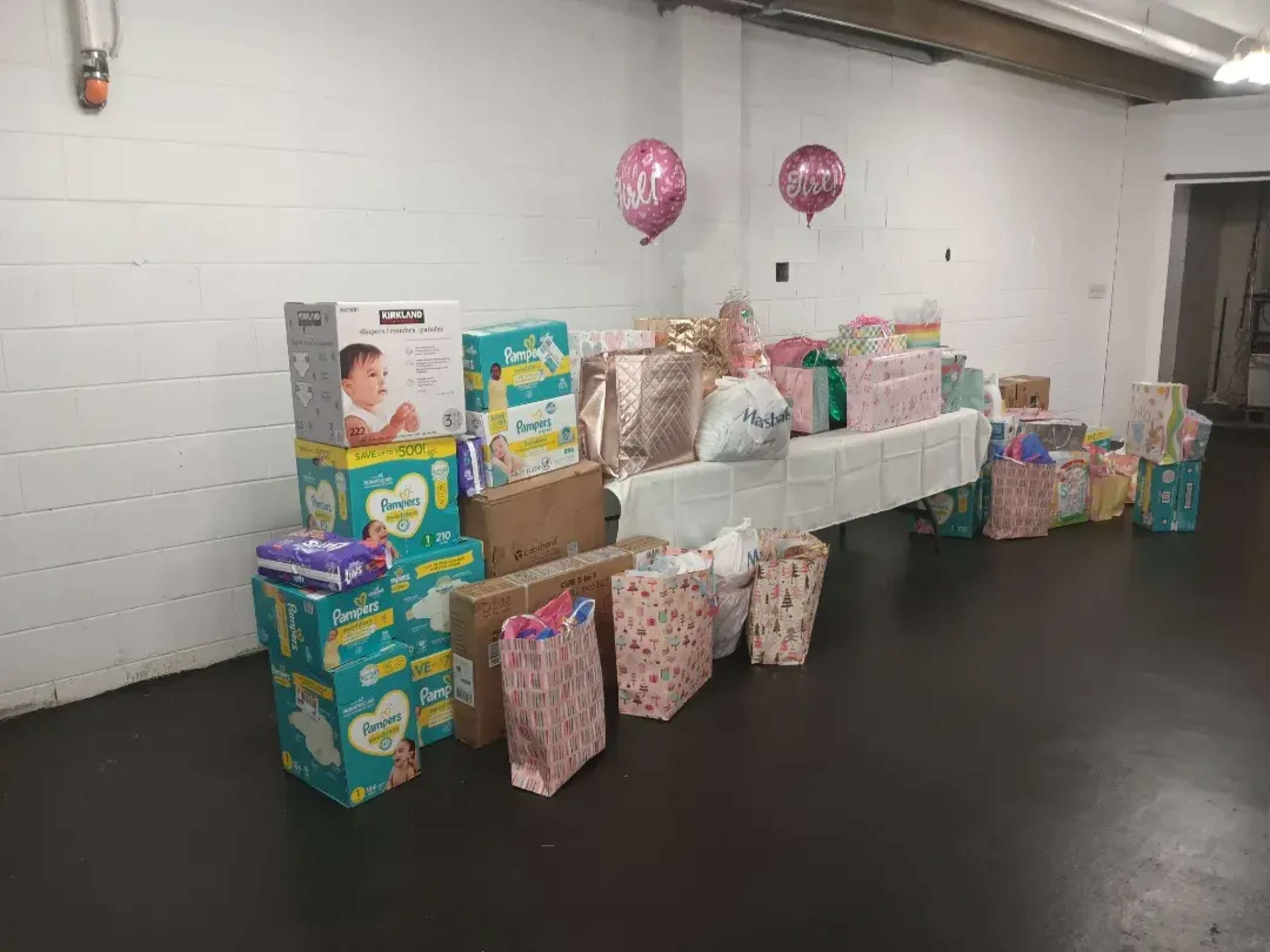 A display of gift packages and boxes, including diapers, arranged on tables in a white-walled room.