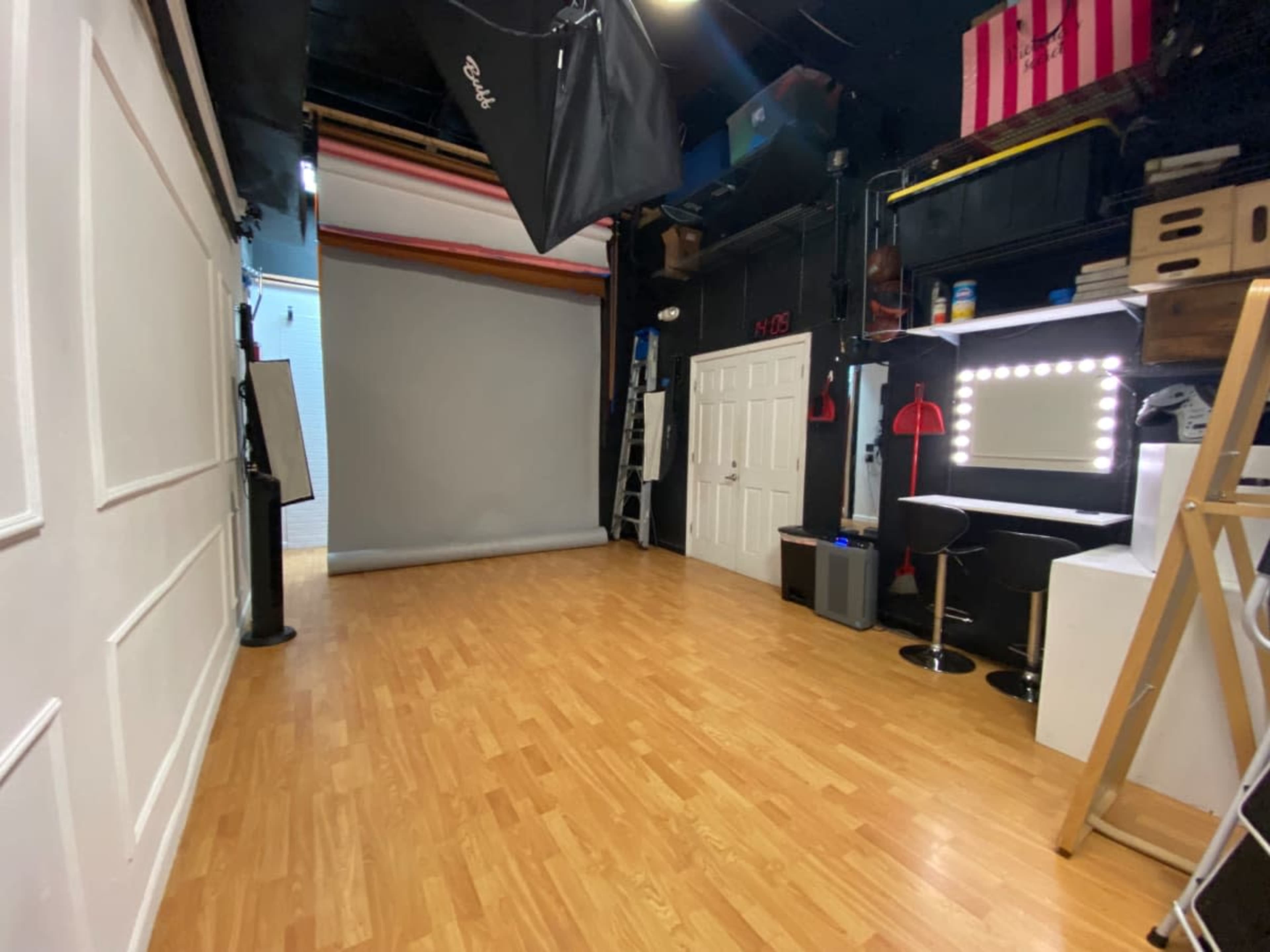 A photography studio with wooden flooring, a grey backdrop, and various lighting equipment along the walls.