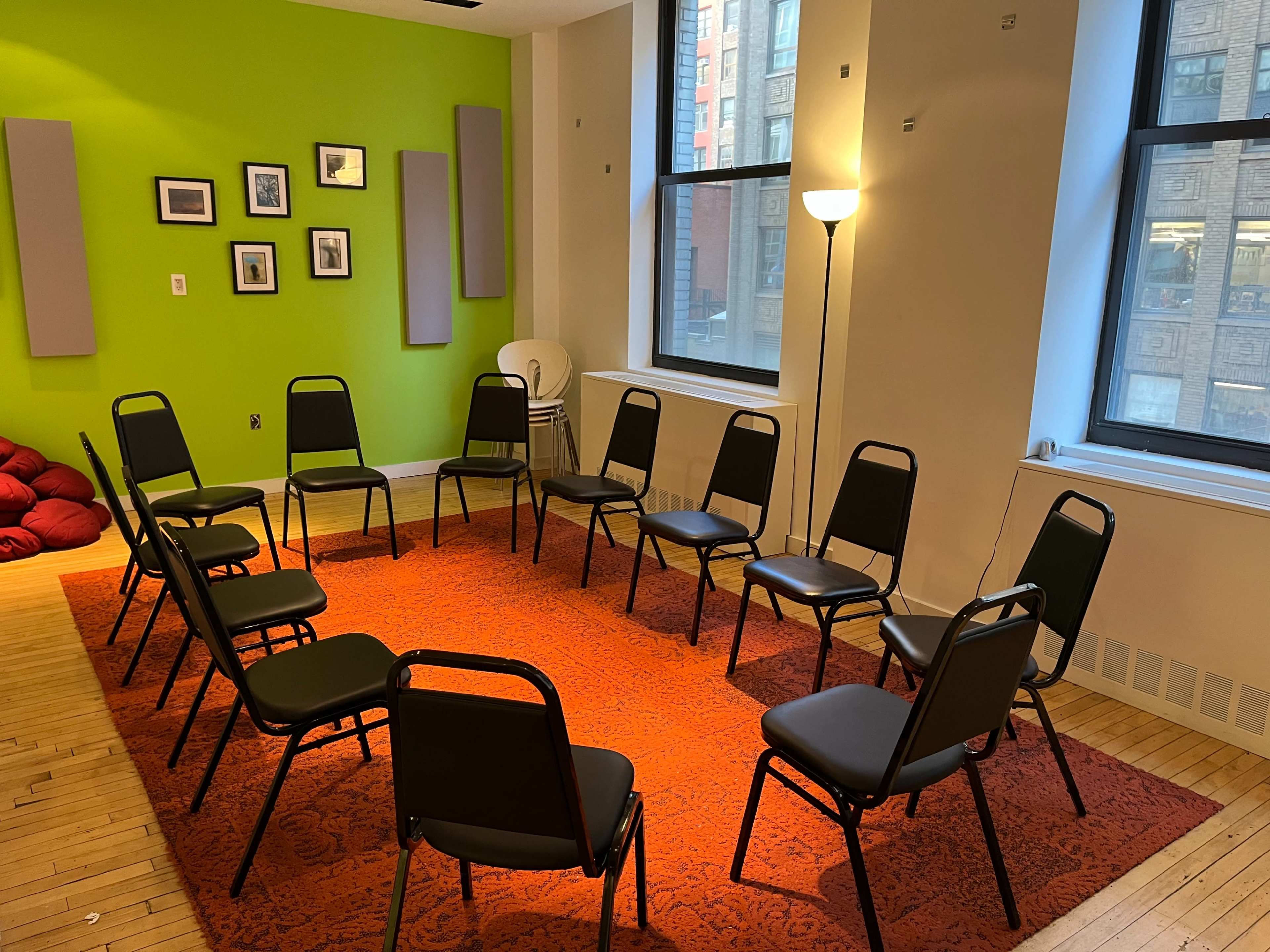 A circle of black chairs is arranged on a patterned rug in a room with green and white walls and large windows.