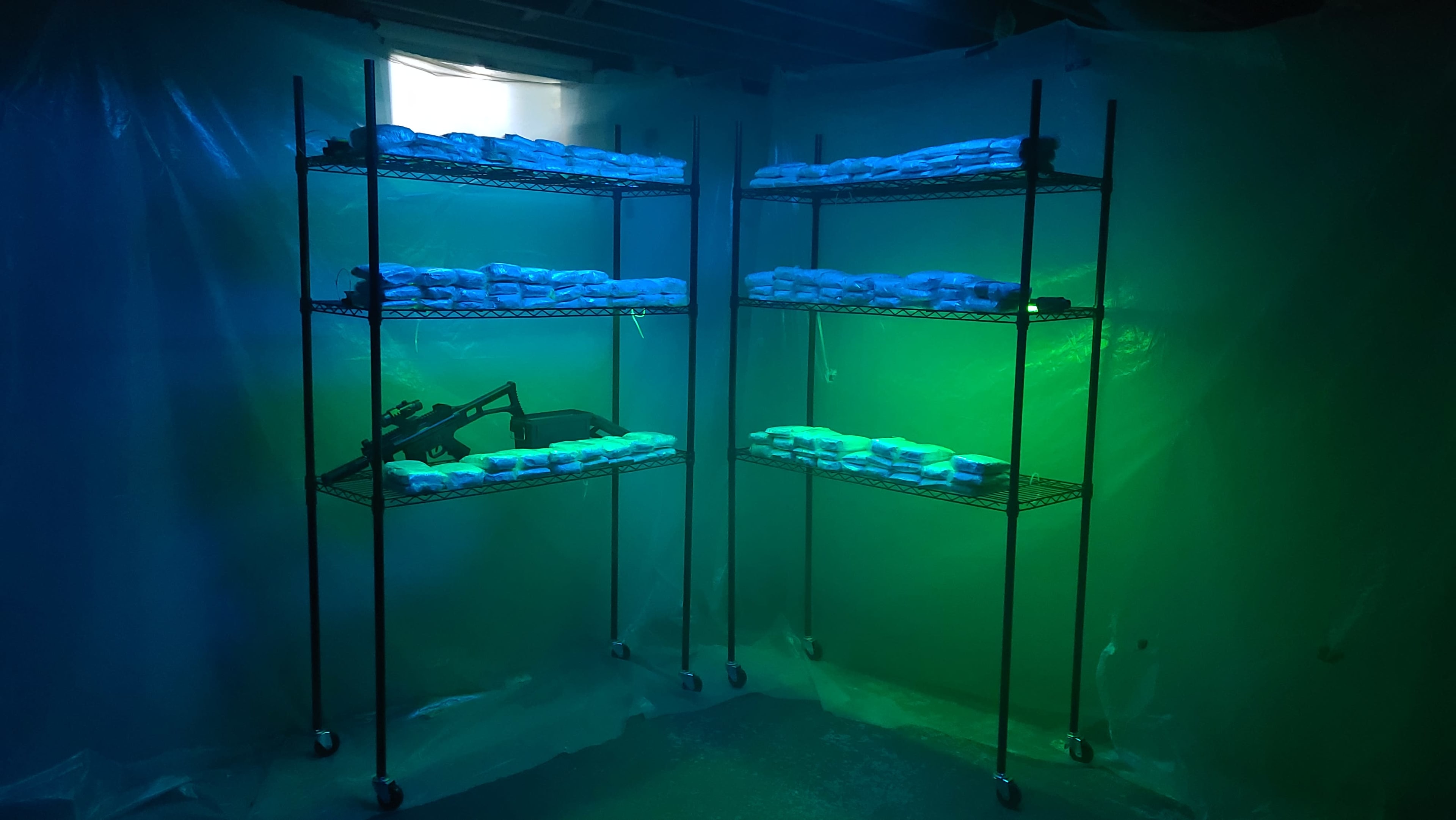 The image shows metal shelves filled with wrapped packages under blue and green lighting in a plastic-covered room.