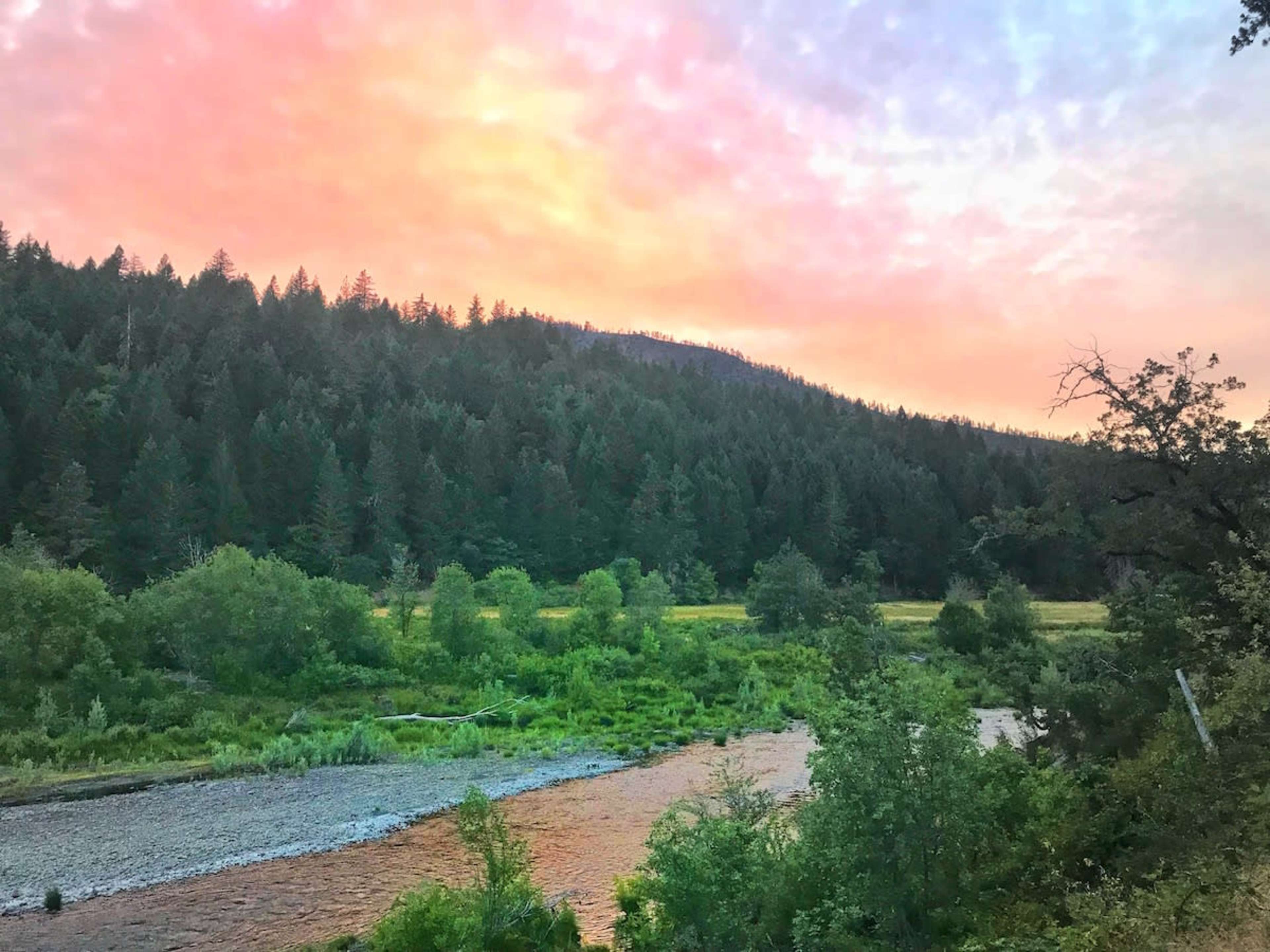 A river flows through a forested landscape under a colorful sky at dusk.