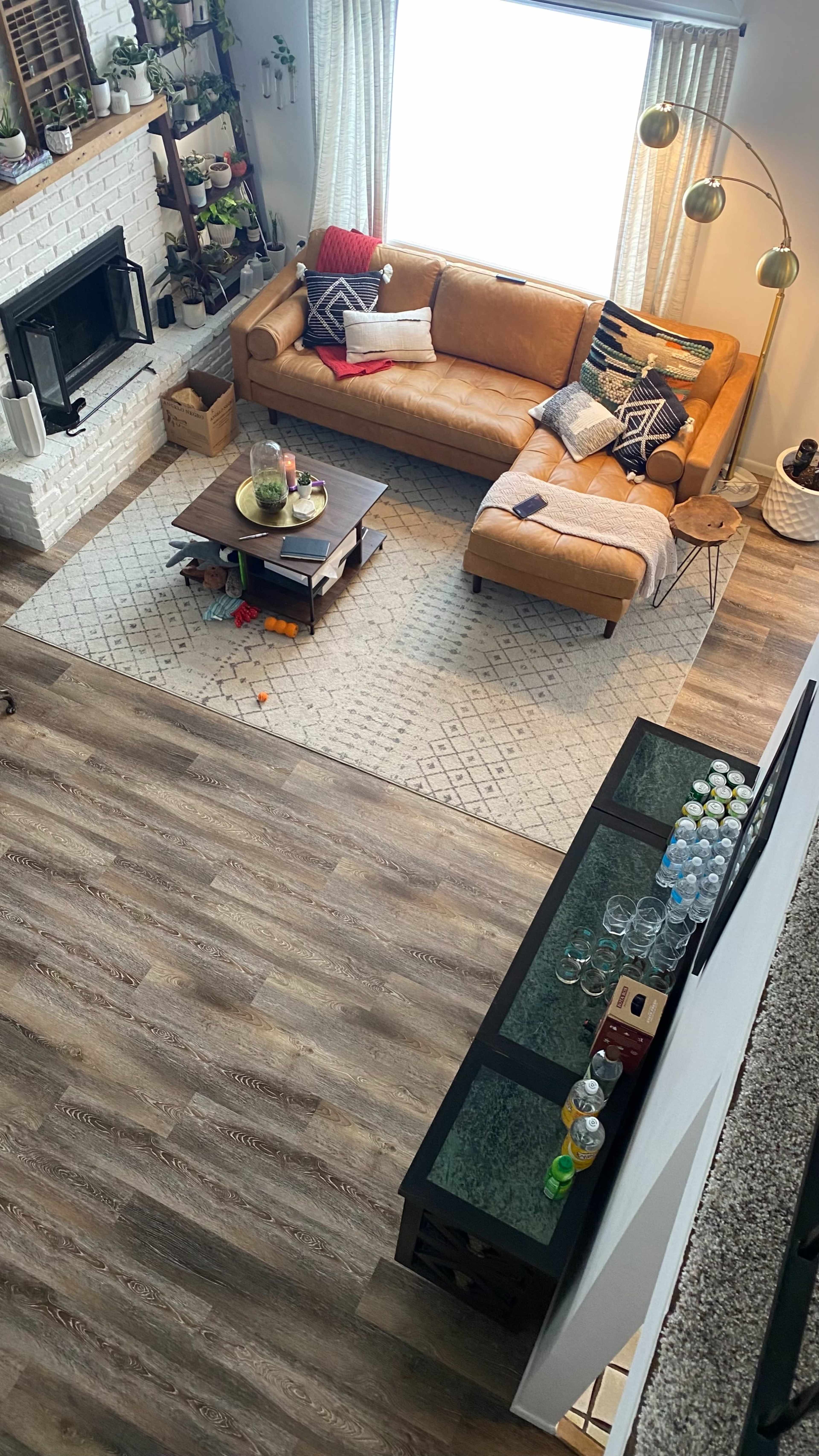 A cozy living room featuring a brown leather sectional sofa, a coffee table, a carpet, and a bar area with drinks, all illuminated by natural light from a large window.