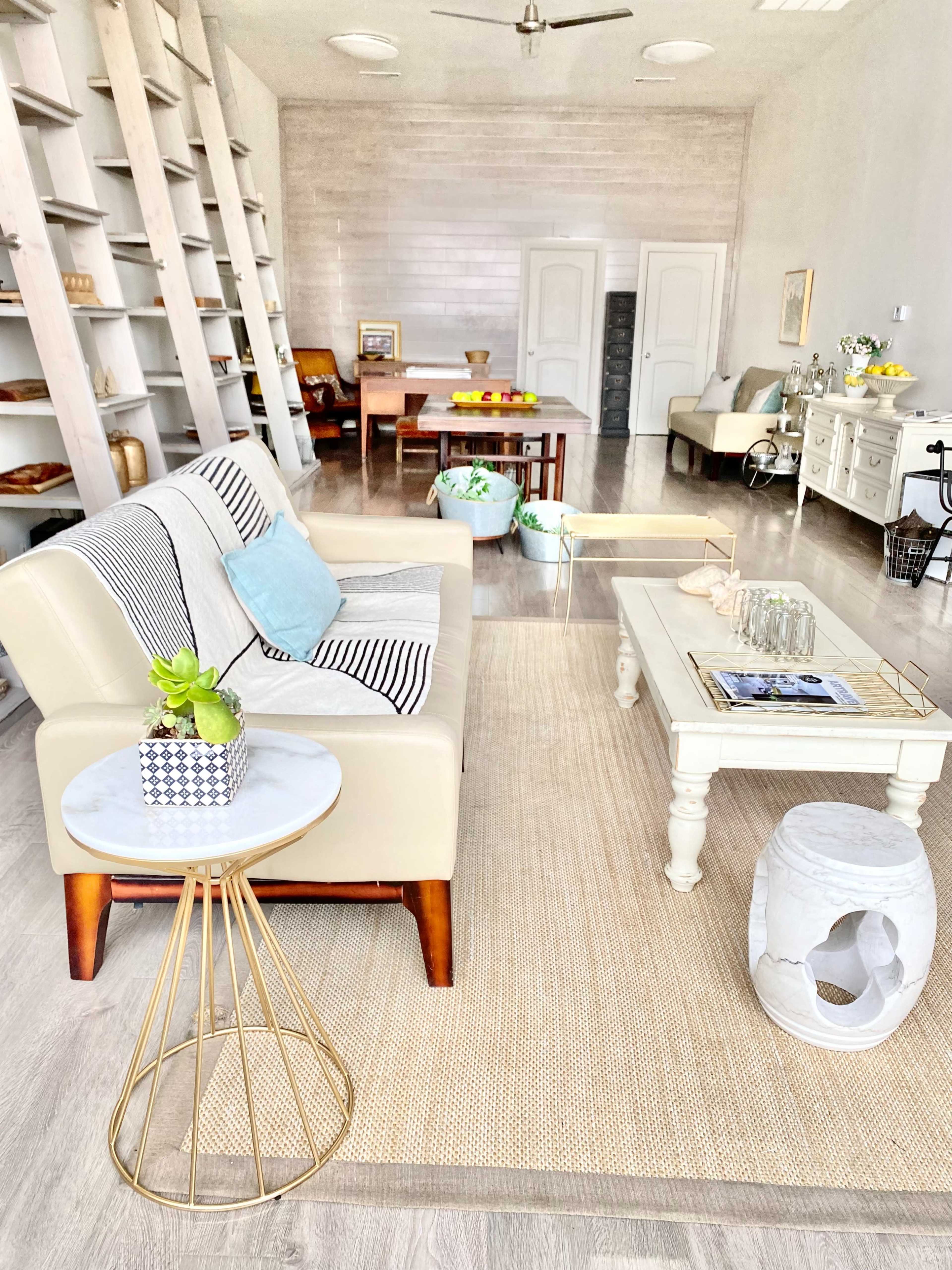 A light and airy living room with a cream-colored sofa, a small coffee table, and wooden shelving holding various decor items.