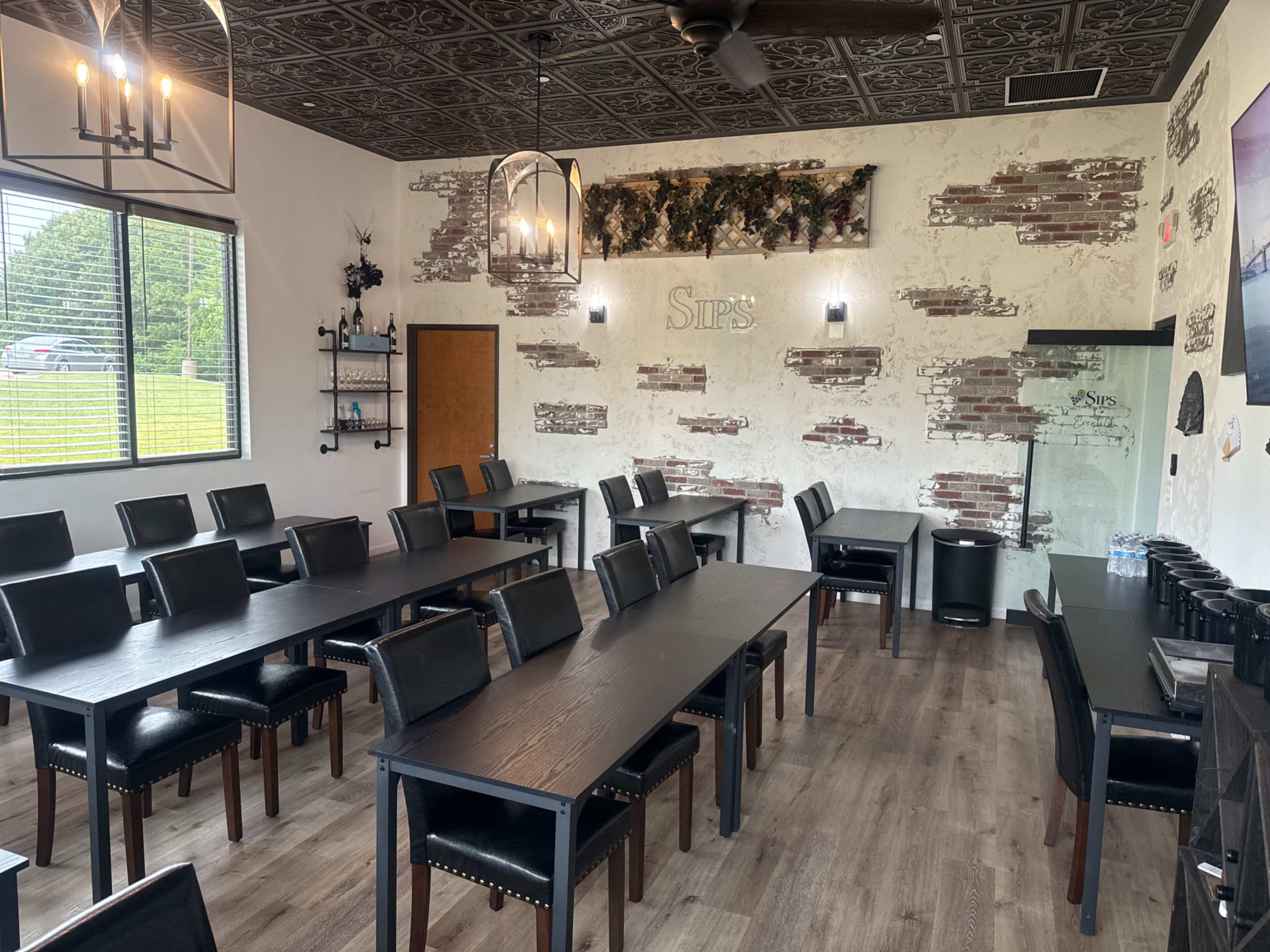 The image shows a modern dining area with dark wooden tables and black leather chairs, featuring exposed brick walls and a ceiling with decorative tiles.