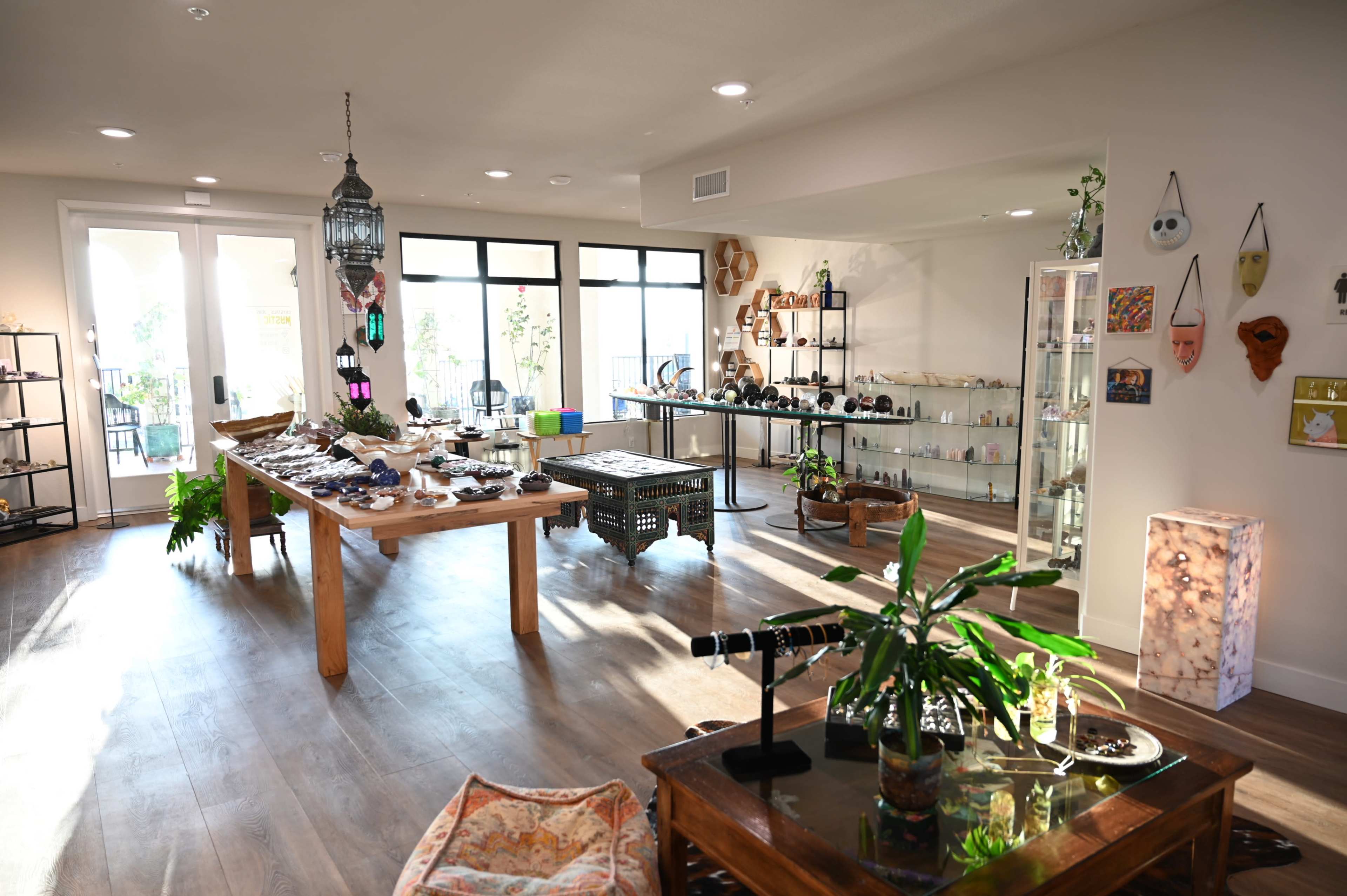 The image shows an open store interior with wooden tables displaying various items, large windows allowing natural light, and shelves lined with products.