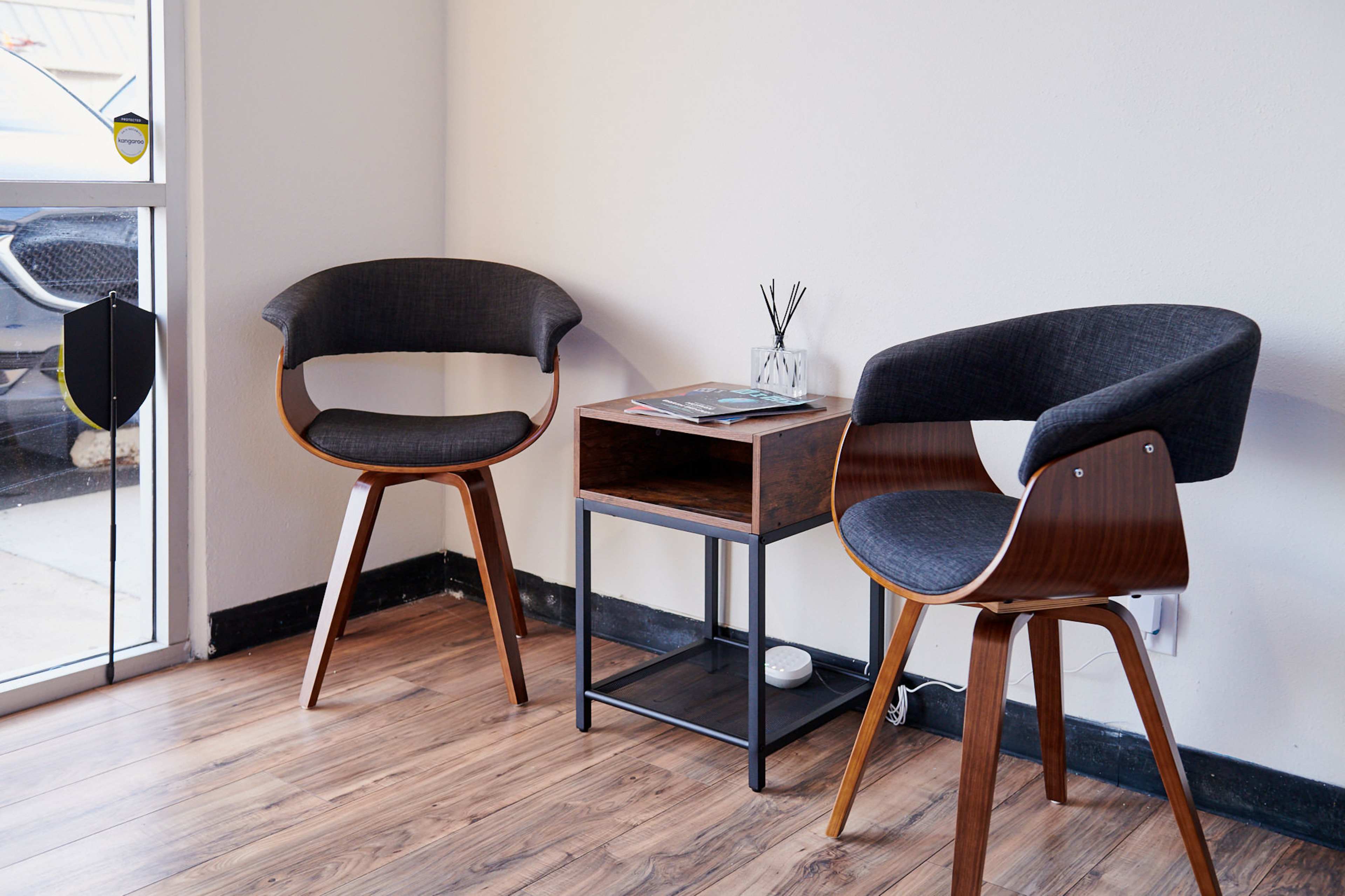 The scene features two modern chairs and a small side table in a well-lit corner of a room with wooden flooring.