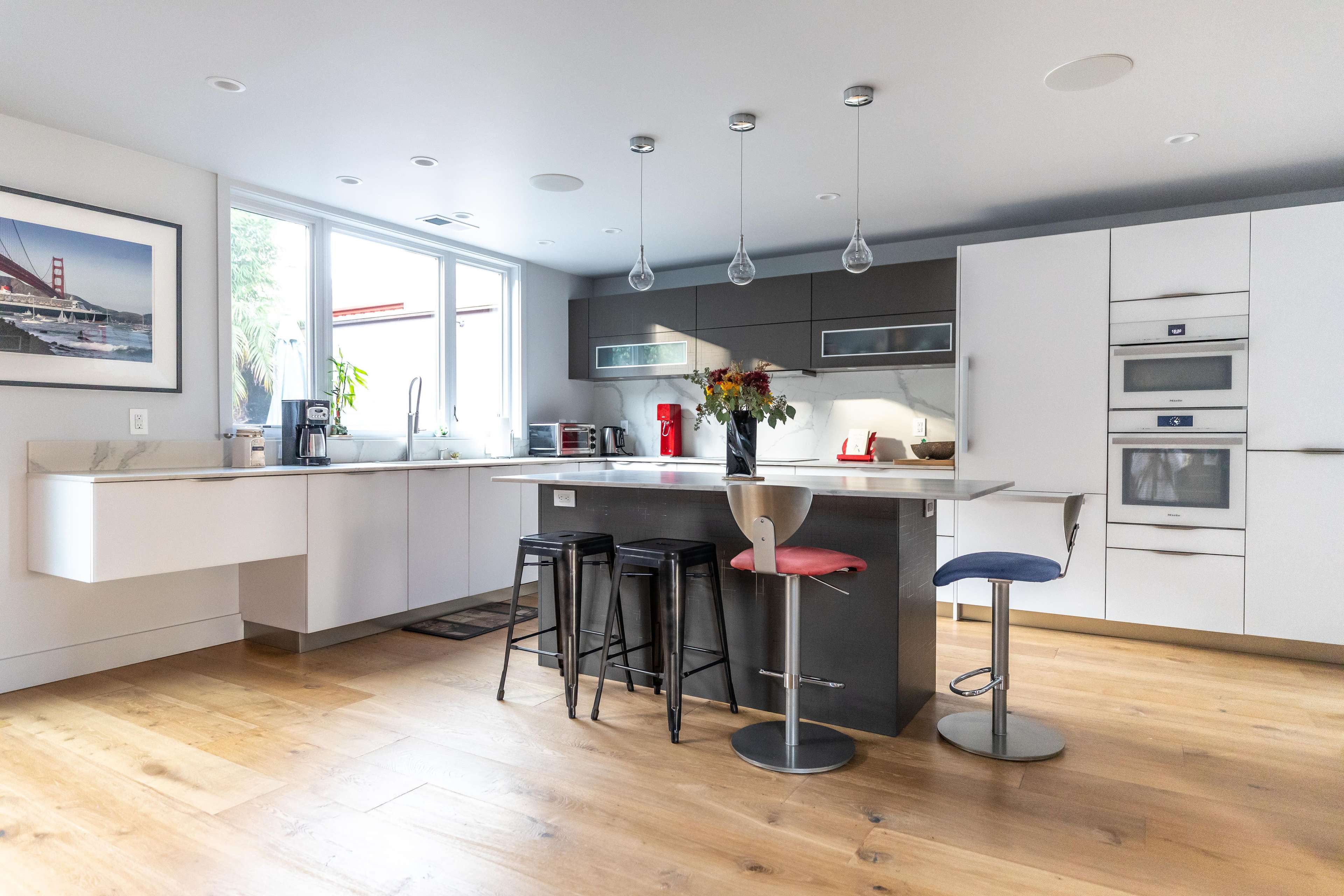 A modern kitchen featuring a central island with seating, sleek cabinetry, and large windows allowing natural light.