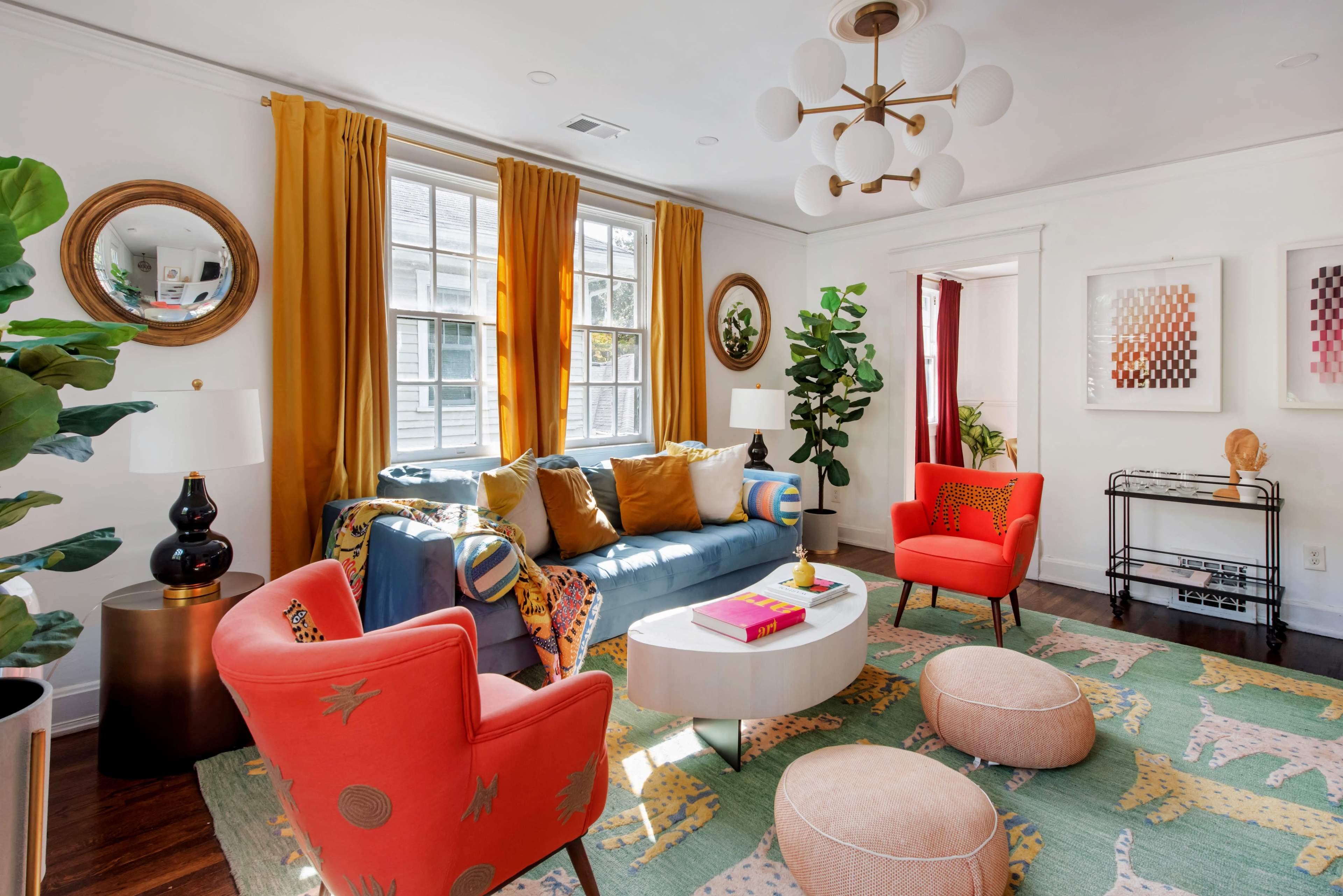 The image depicts a bright, modern living room with a blue sofa, vibrant chairs, and various decorative elements including plants and artwork.