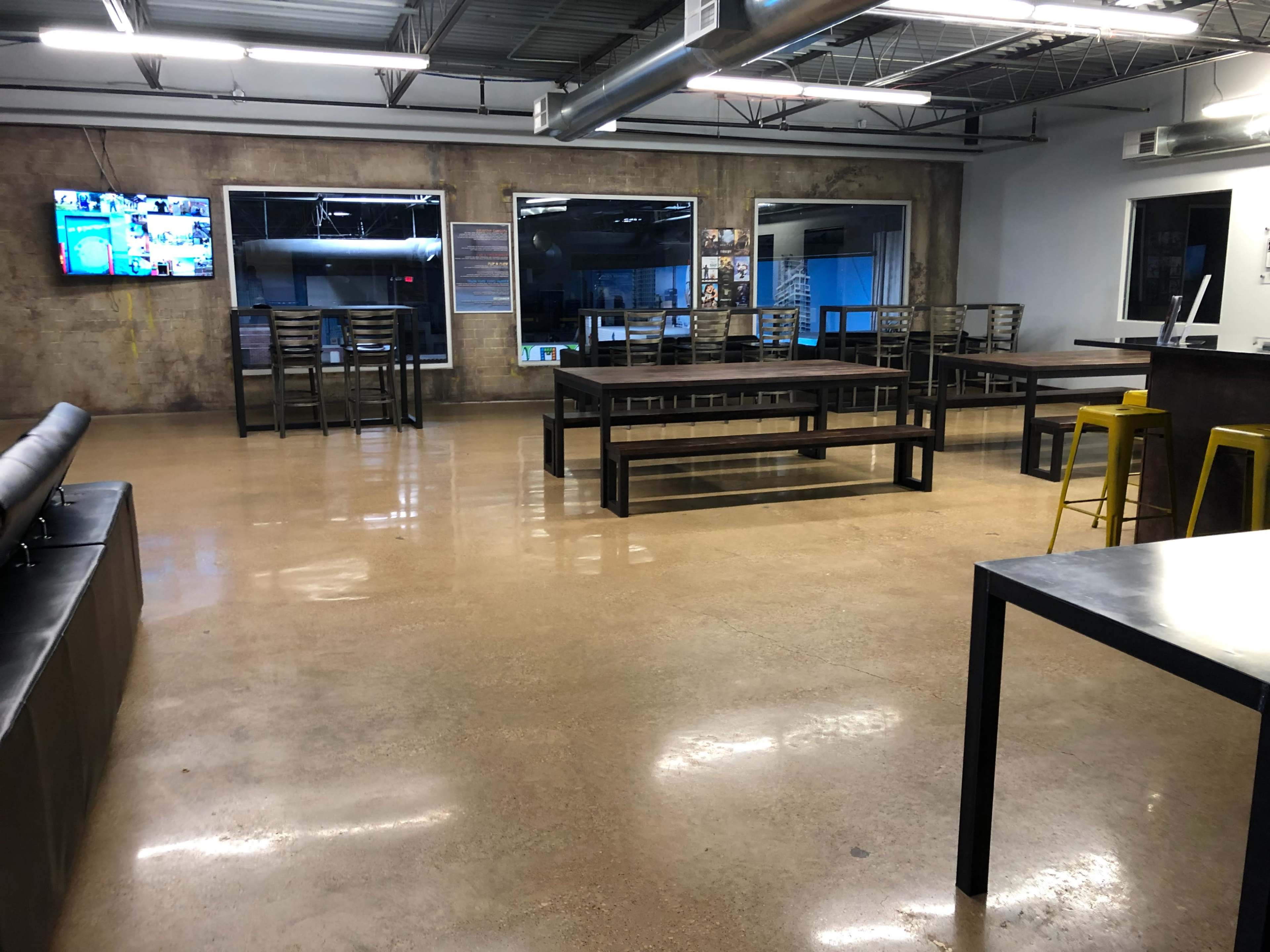An empty industrial-style indoor space with concrete floors, metal tables, and a large screen displaying various images on one wall.