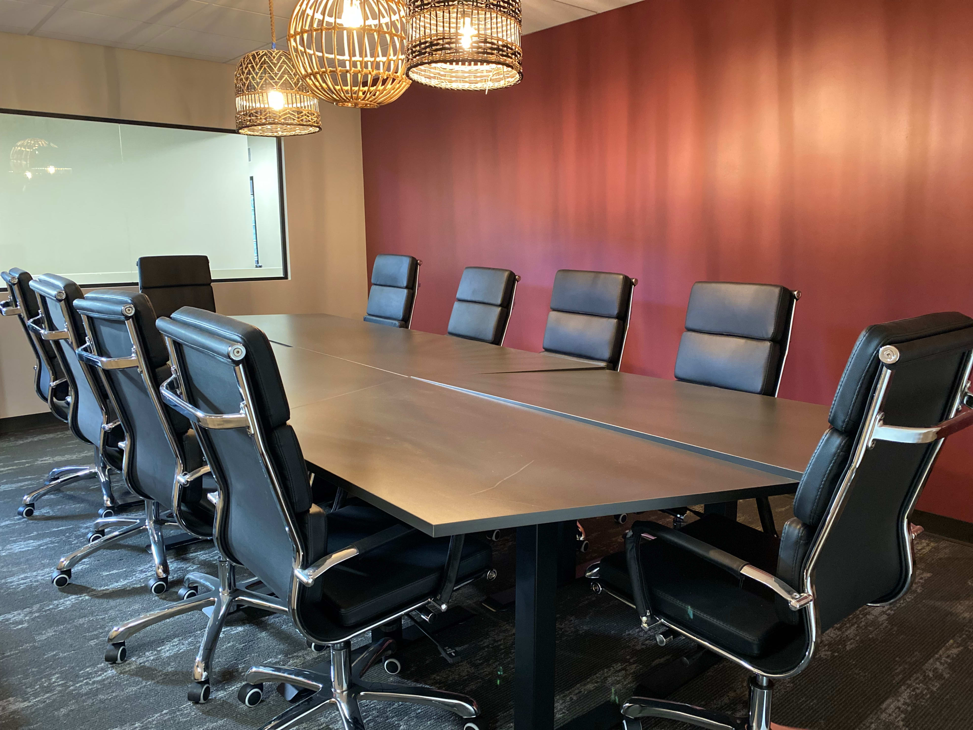 A large, modern conference room features a long table surrounded by black leather office chairs under pendant lights.