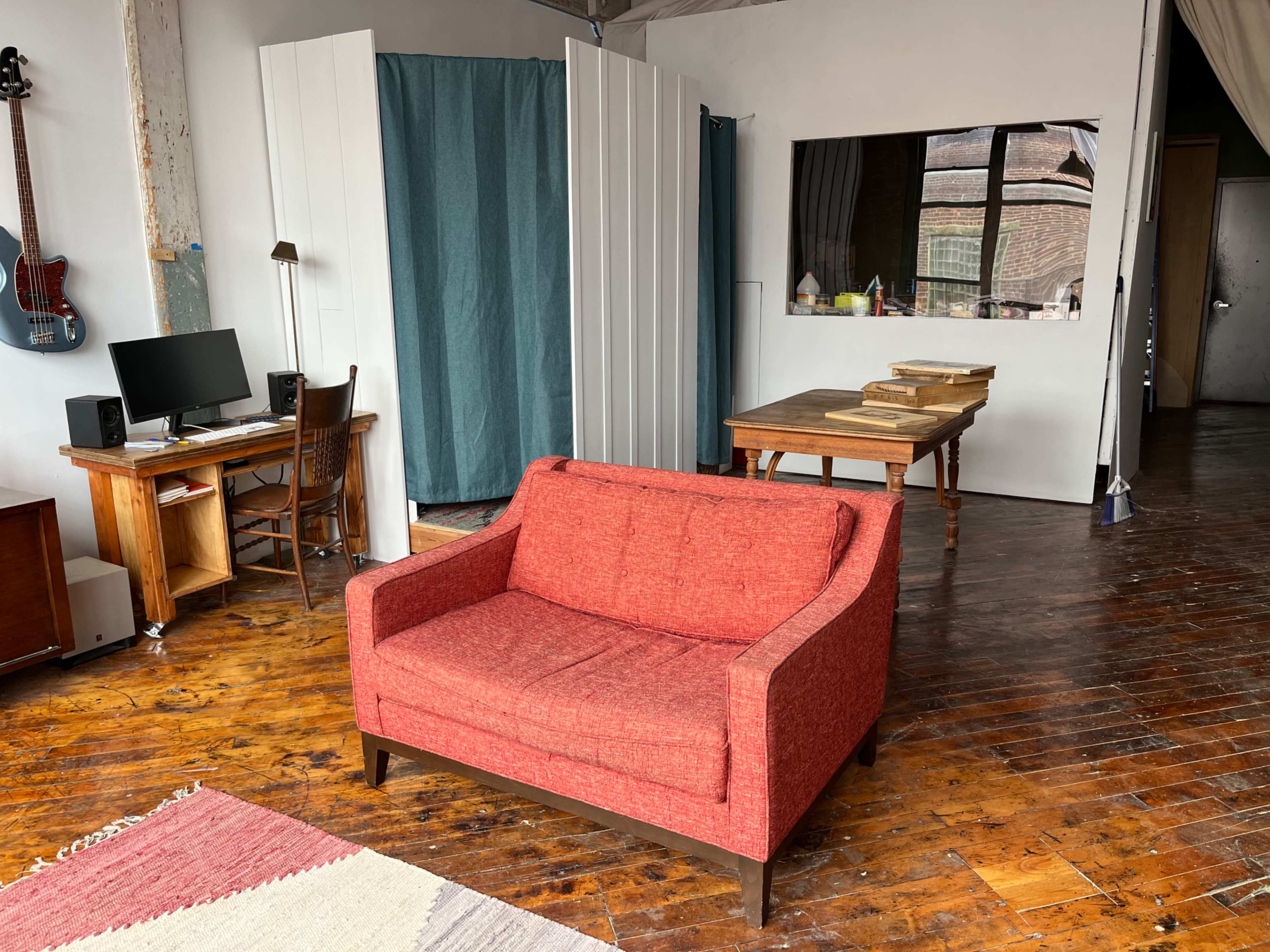 A spacious interior with a red couch centered in the room, a desk with a computer on one side, and a wooden table against a wall.