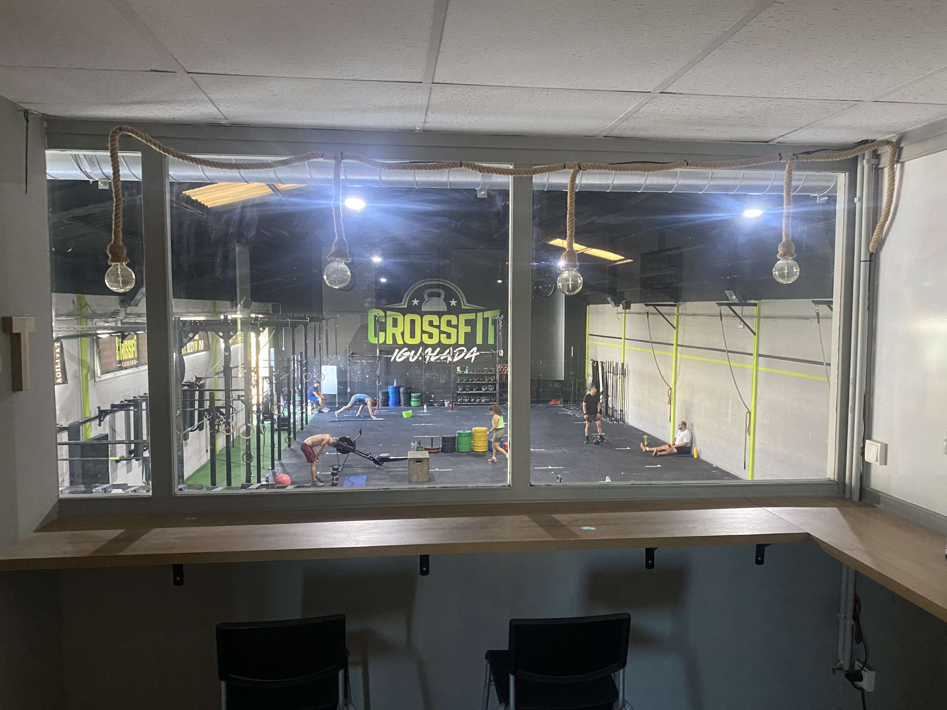 A view from a window shows a CrossFit gym with athletes working out on various equipment.
