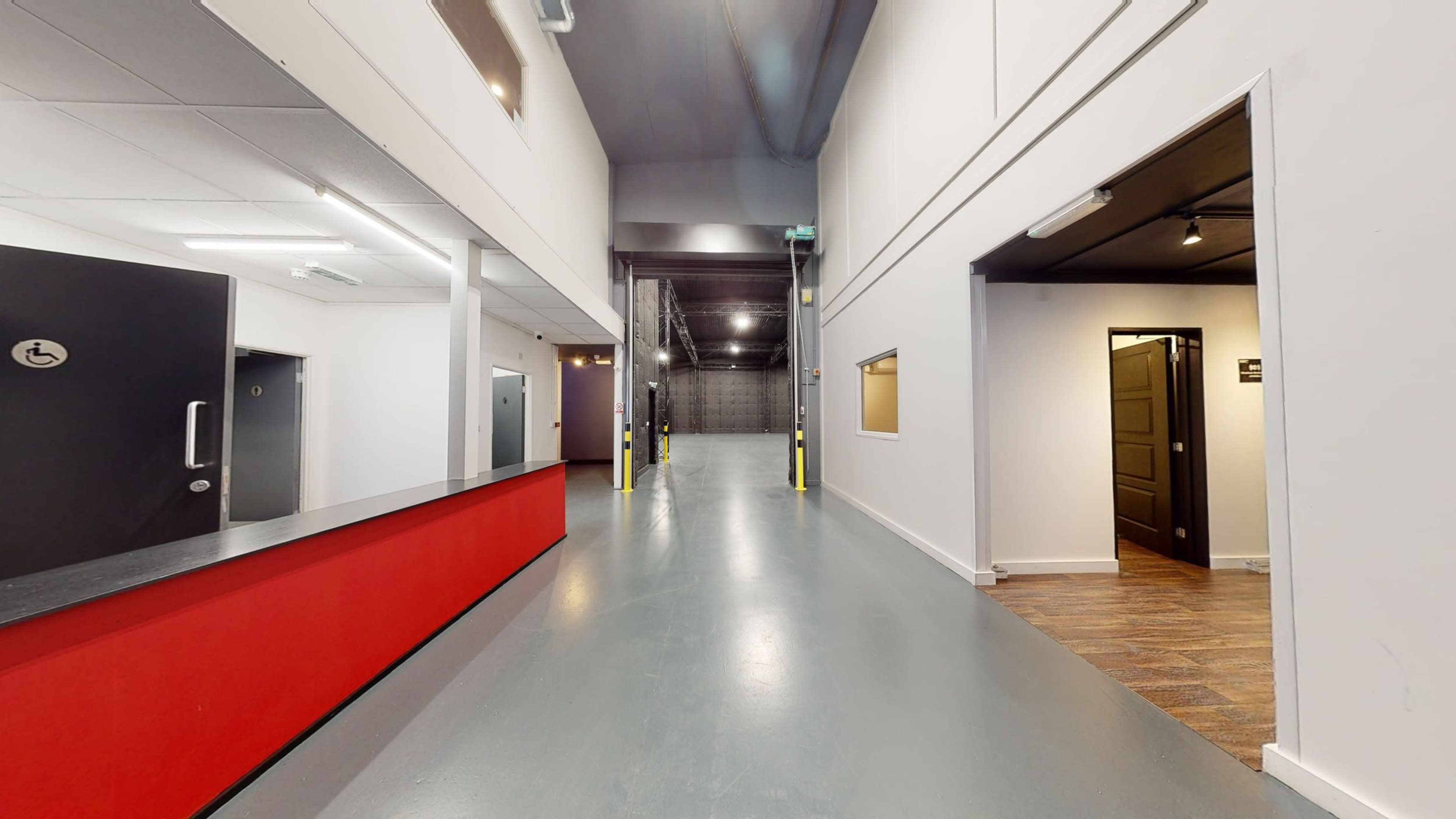 A spacious hallway with a red reception desk on the left, leading to stairs at the back and doors on the right.