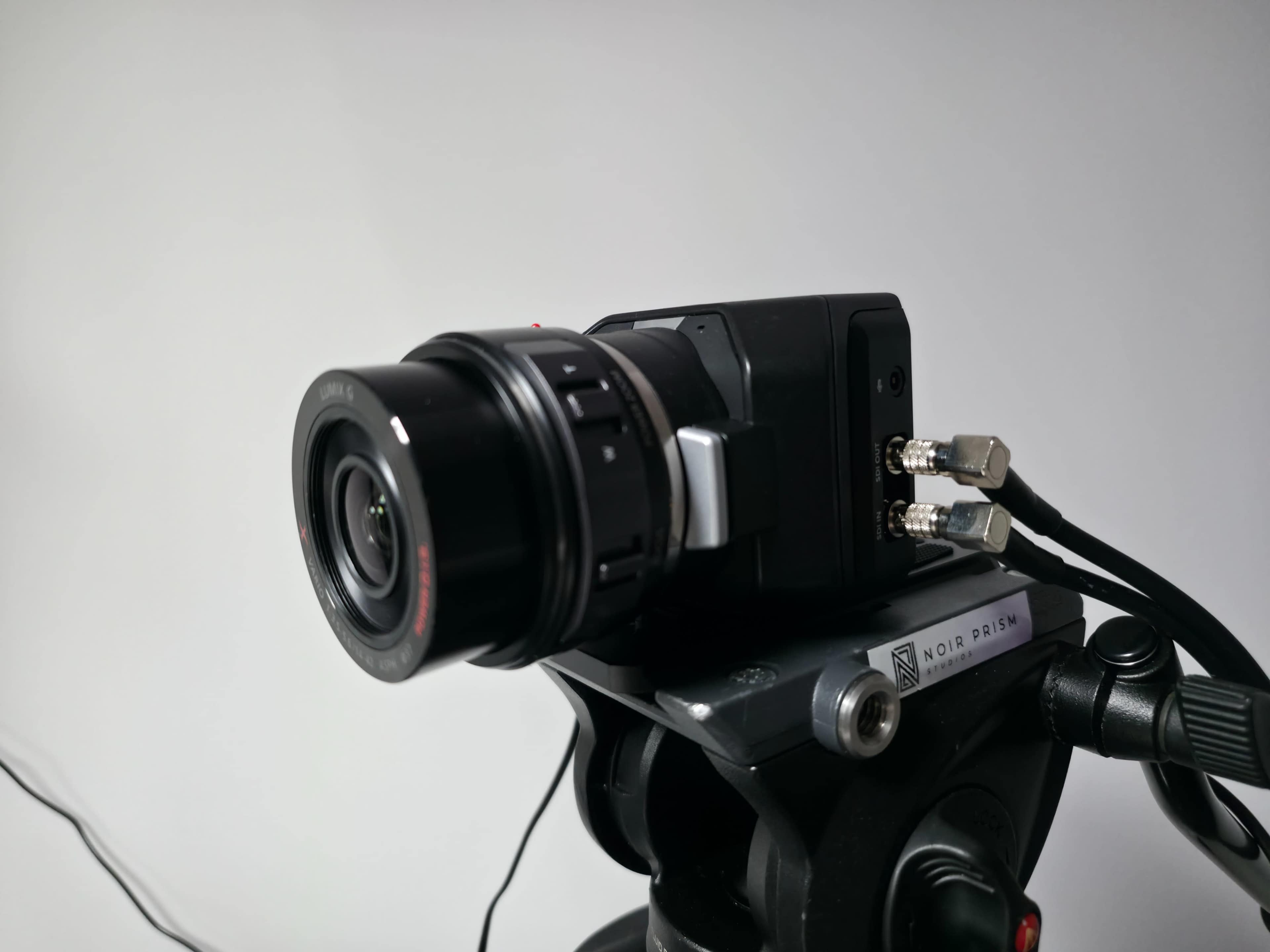 The image shows a camera mounted on a tripod with a lens and cables connected to it.
