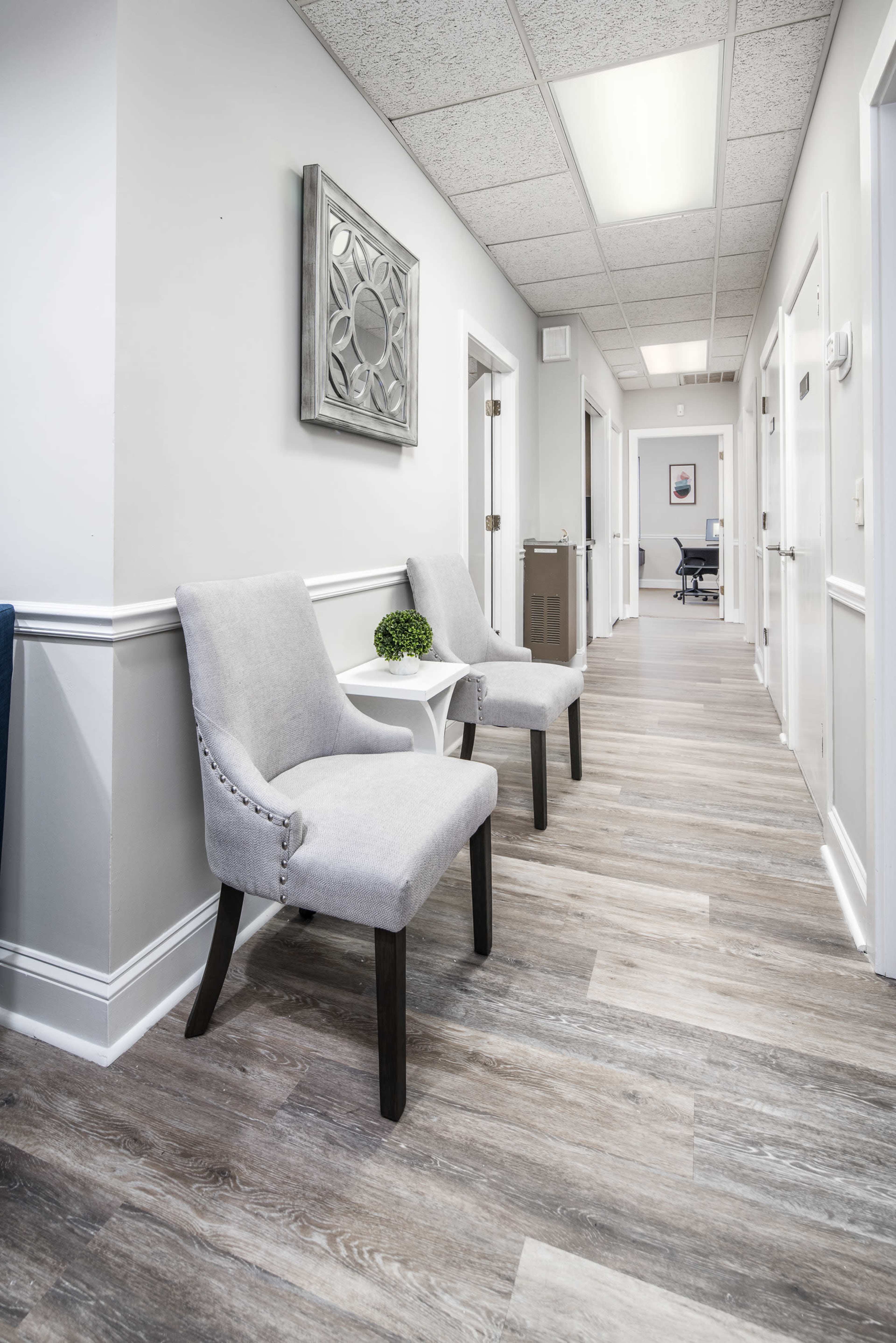 A clean hallway with two gray chairs, a small table between them, and doors leading to other rooms on either side.
