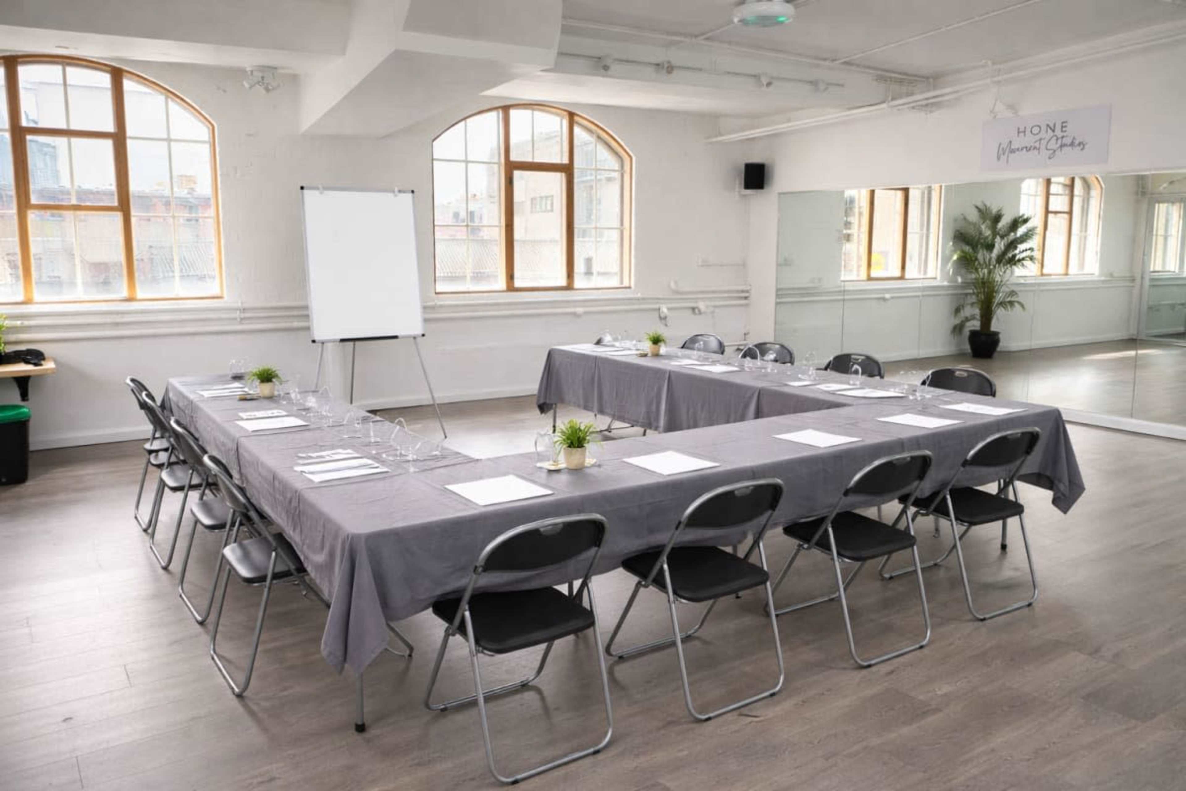 A modern conference room features a long table surrounded by chairs, with a whiteboard and large windows allowing natural light to enter.