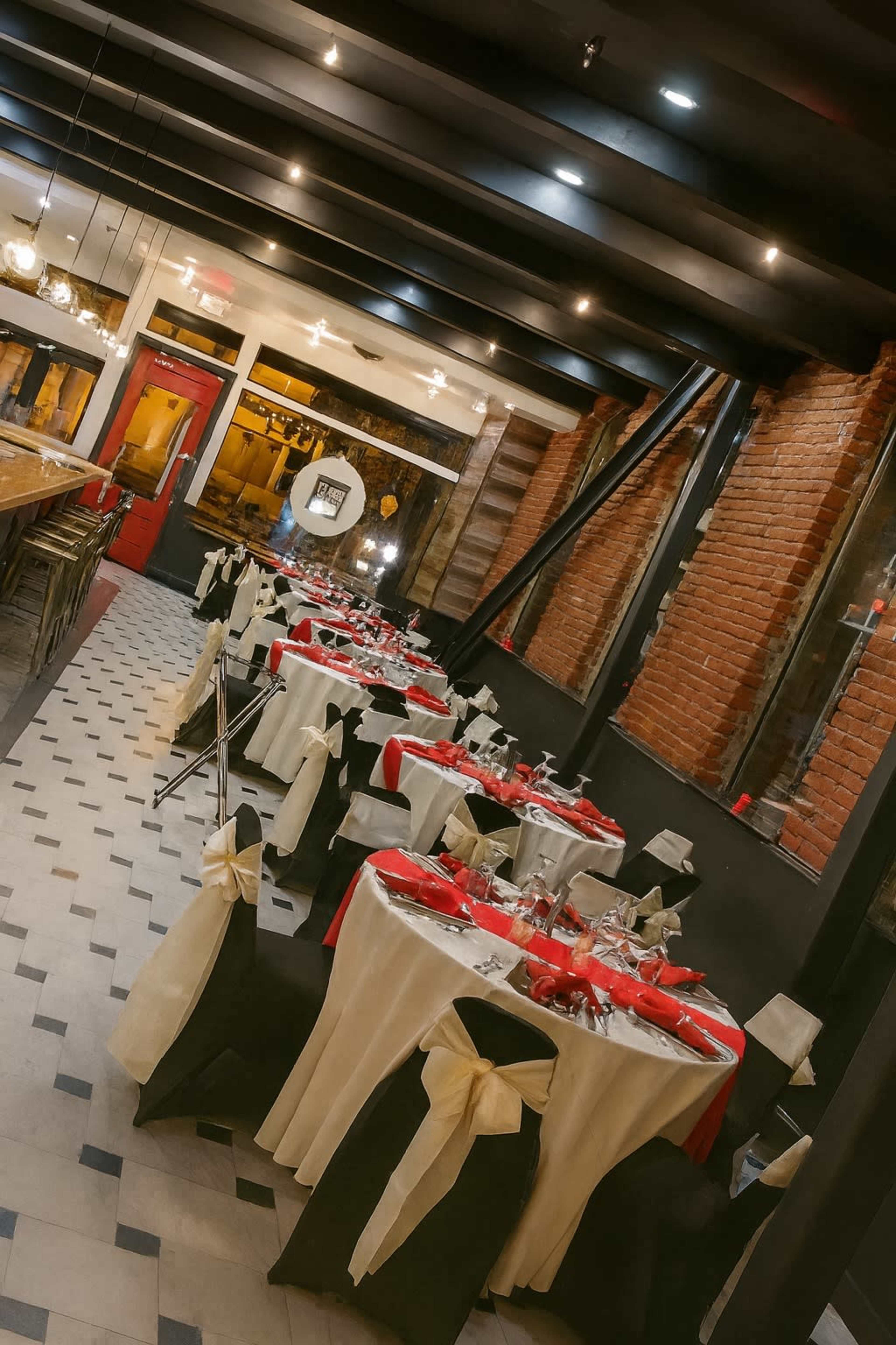 The image shows a restaurant interior with elegantly set tables adorned with red and black tablecloths and chairs featuring coordinating sashes.