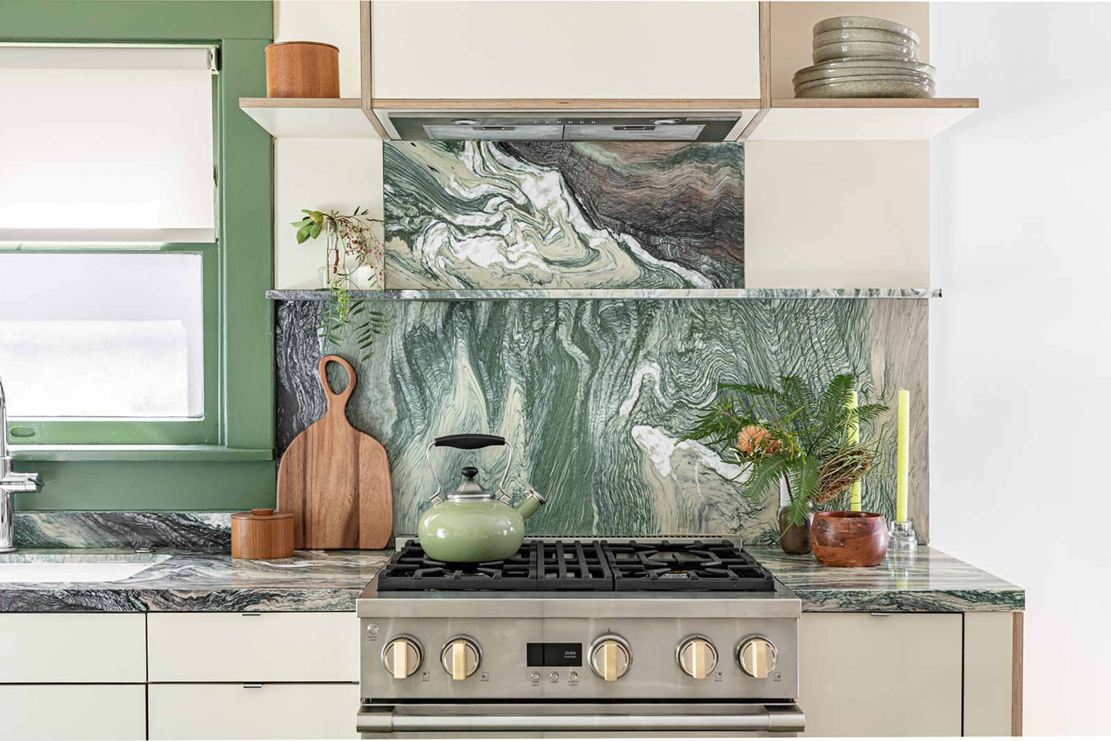 A modern kitchen with a green and marble-patterned backsplash, a stainless steel stove, and wooden accents.