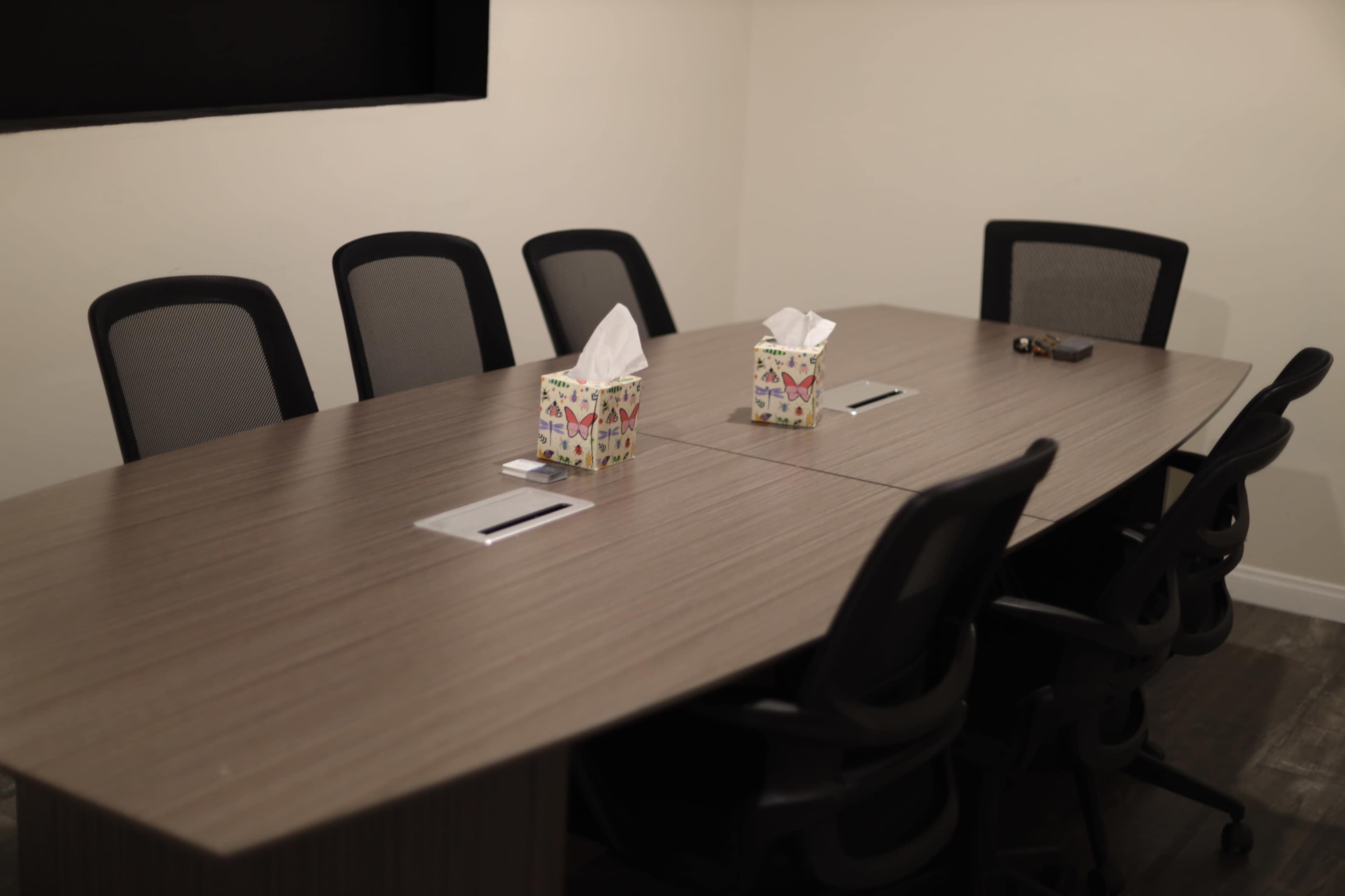 A conference table is set with two tissue boxes and several chairs arranged around it in a meeting room.