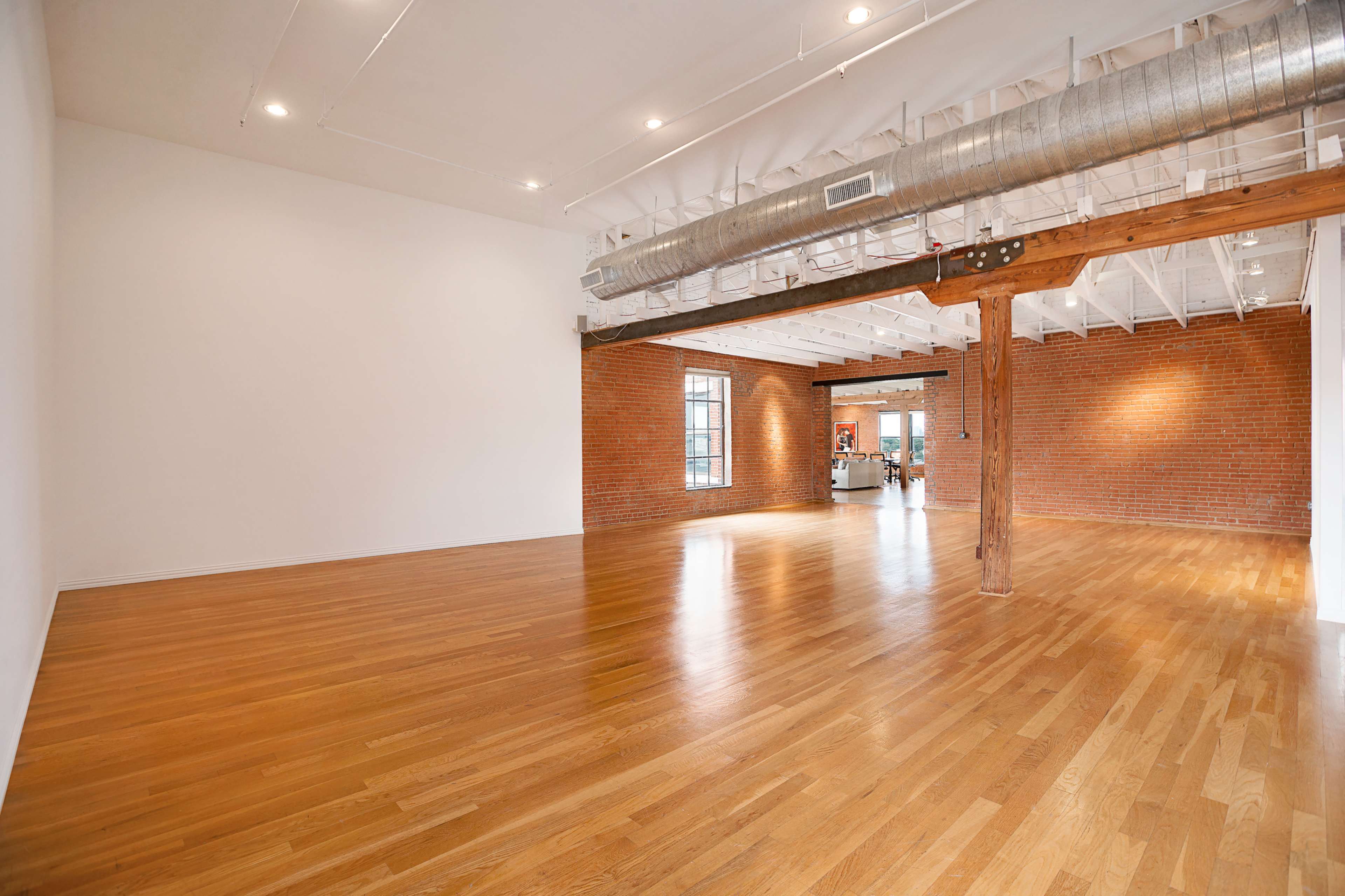 A spacious, empty room with hardwood flooring and a combination of white and exposed brick walls.