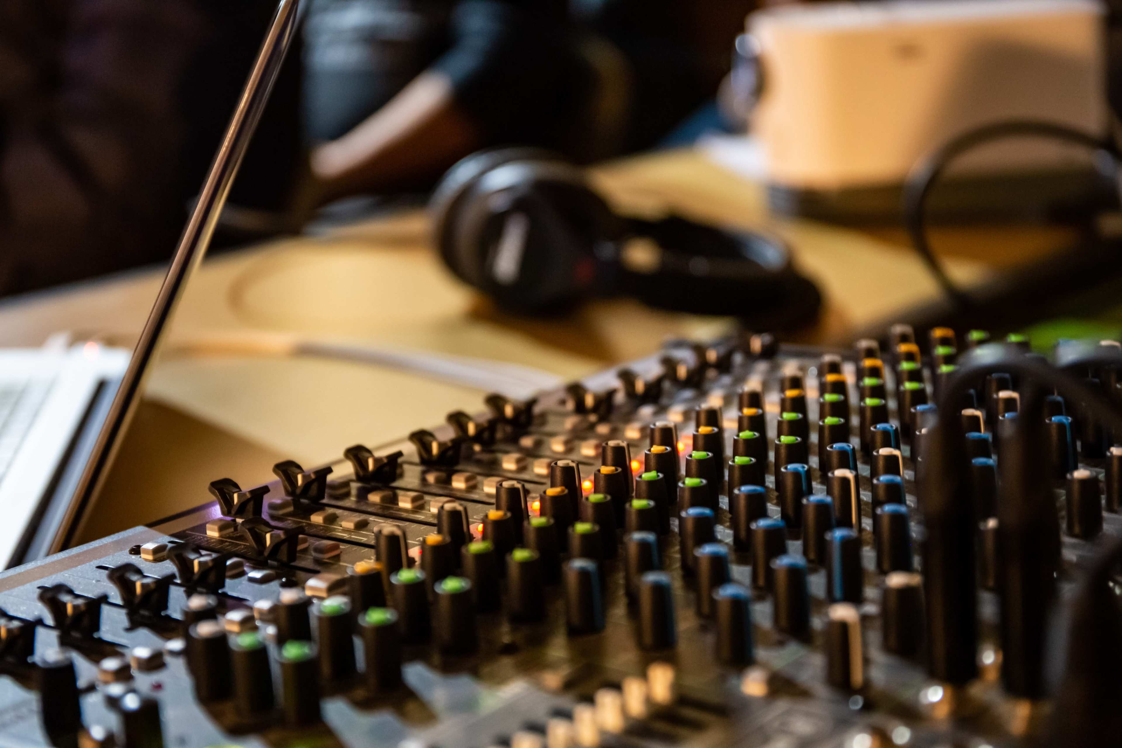 A close-up of a sound mixing console with colored knobs and sliders, accompanied by a pair of headphones in the background.
