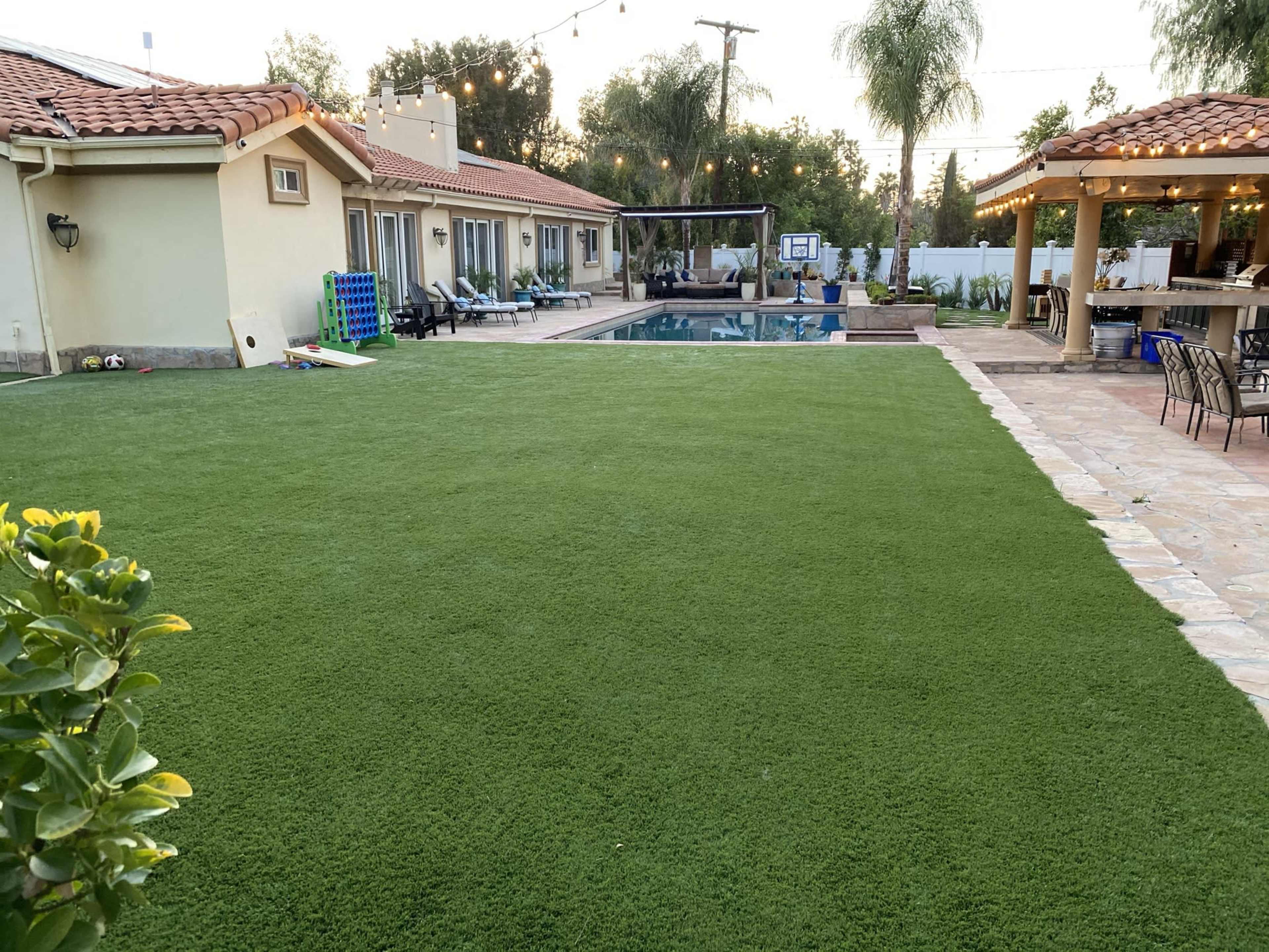 A backyard with a well-maintained green lawn, a swimming pool, and a patio area with string lights.