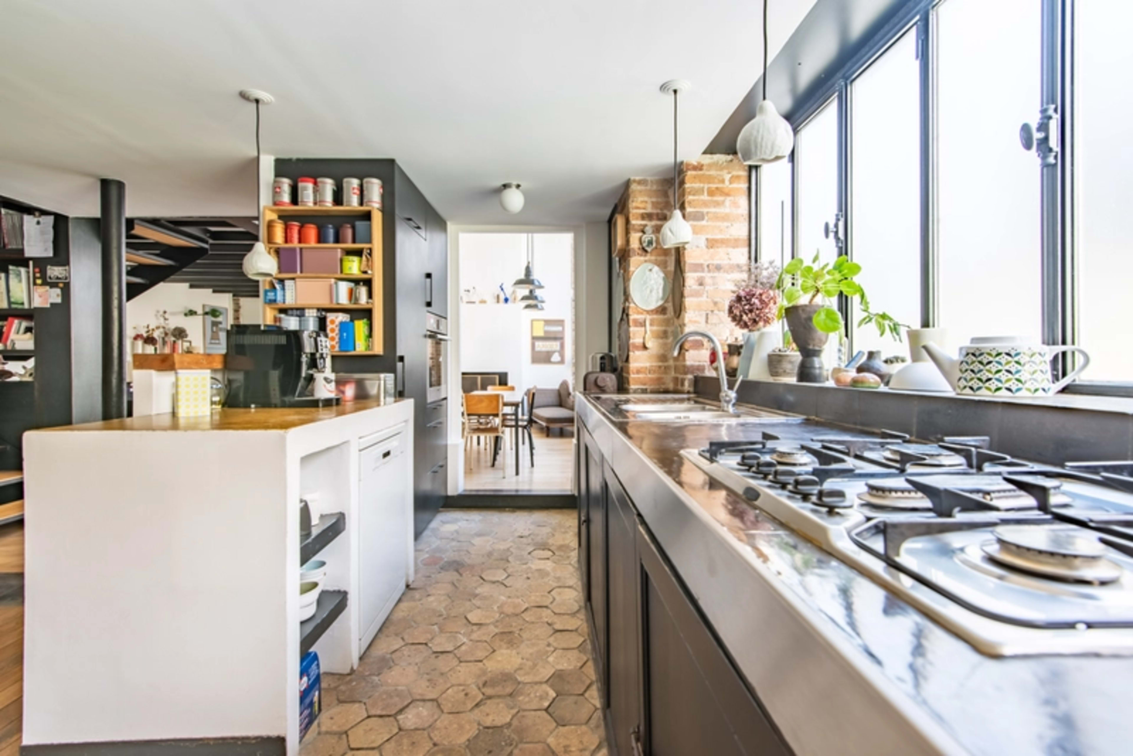 A modern kitchen features a central island with a gas stove, large windows providing natural light, and a view of a dining area.