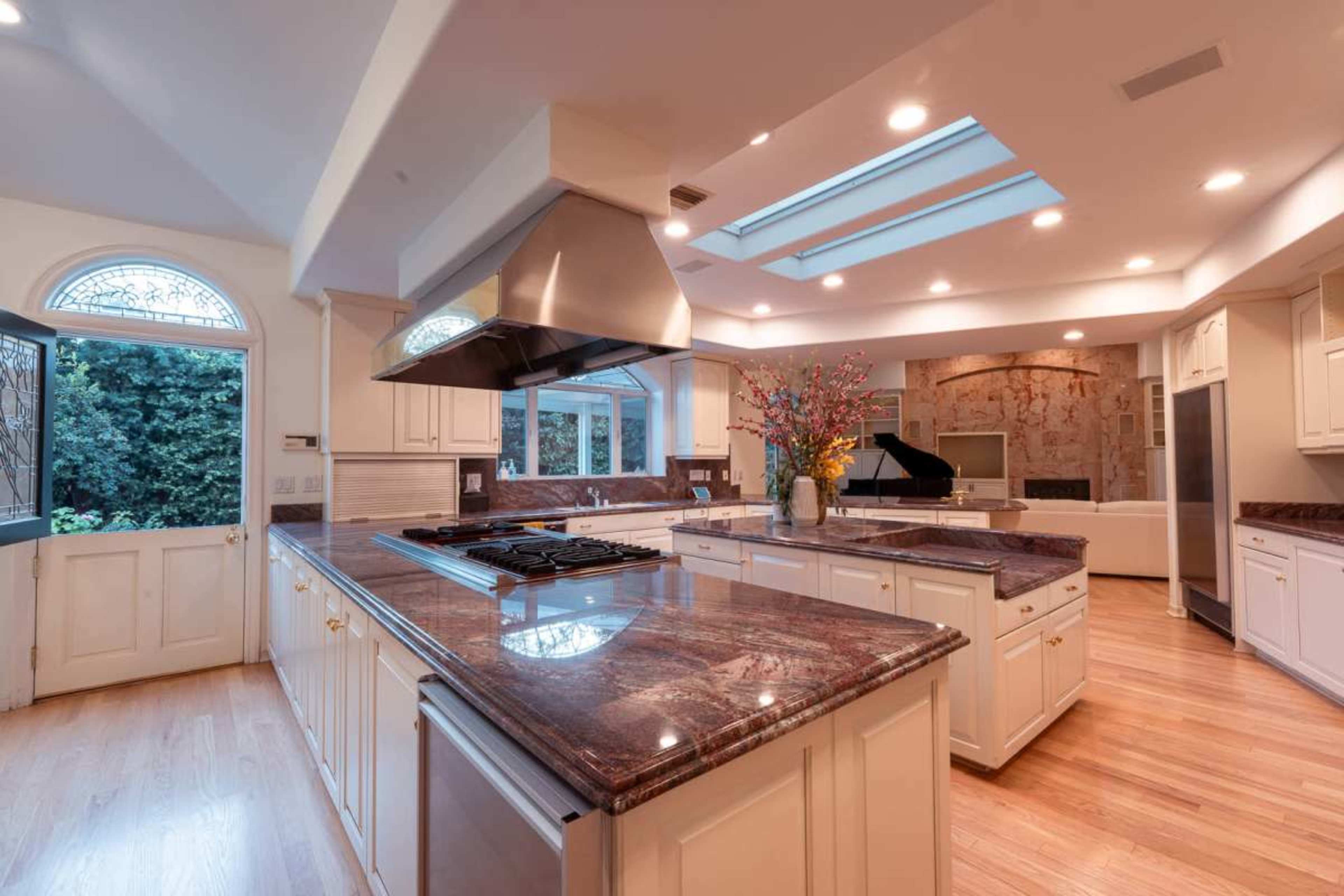 A spacious kitchen features white cabinetry, a large central island with a gas cooktop, and natural light streaming in through skylights and windows.