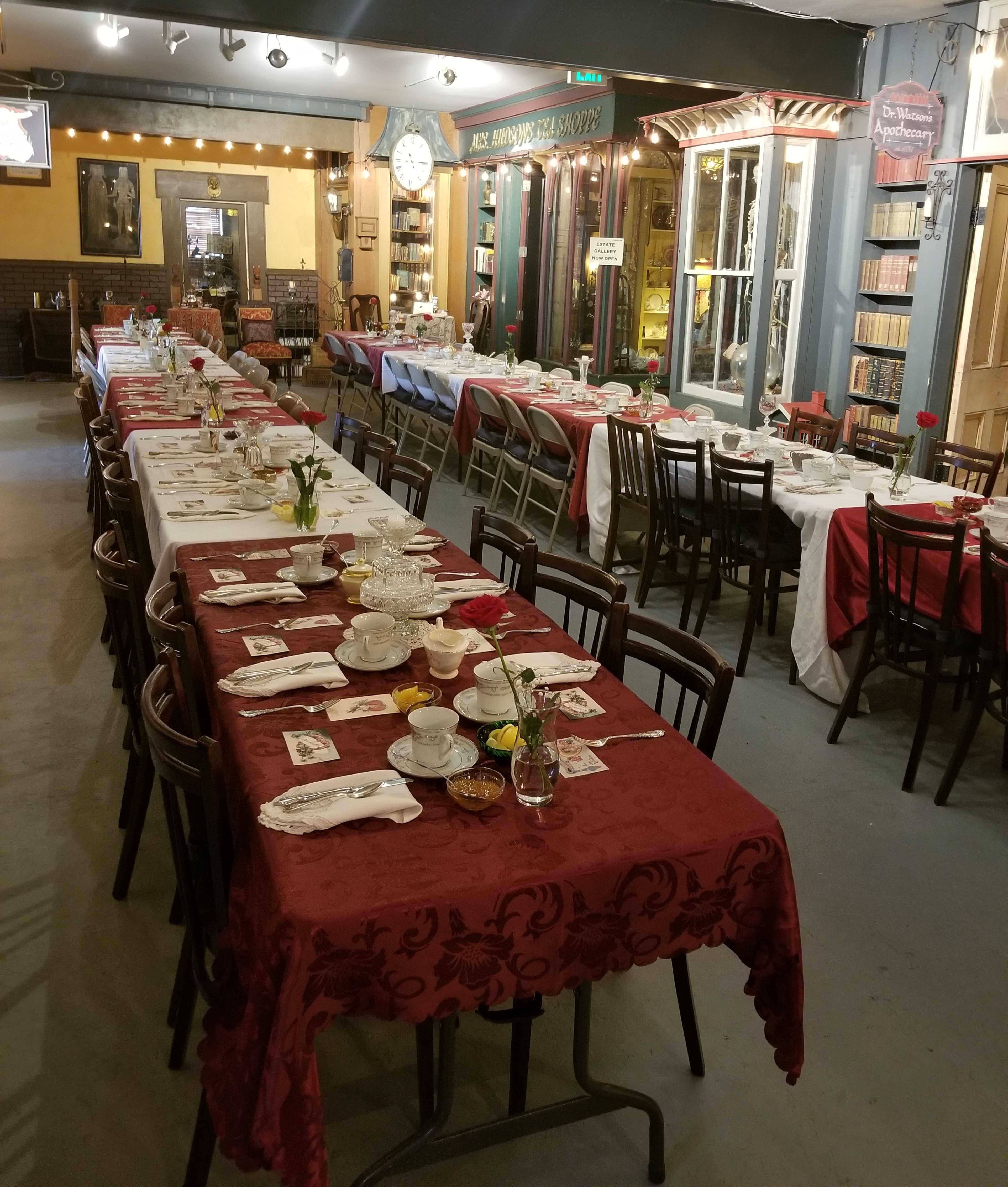 A dining area arranged with long tables covered in red and white tablecloths, set for a meal with dishes, utensils, and small flower centerpieces.