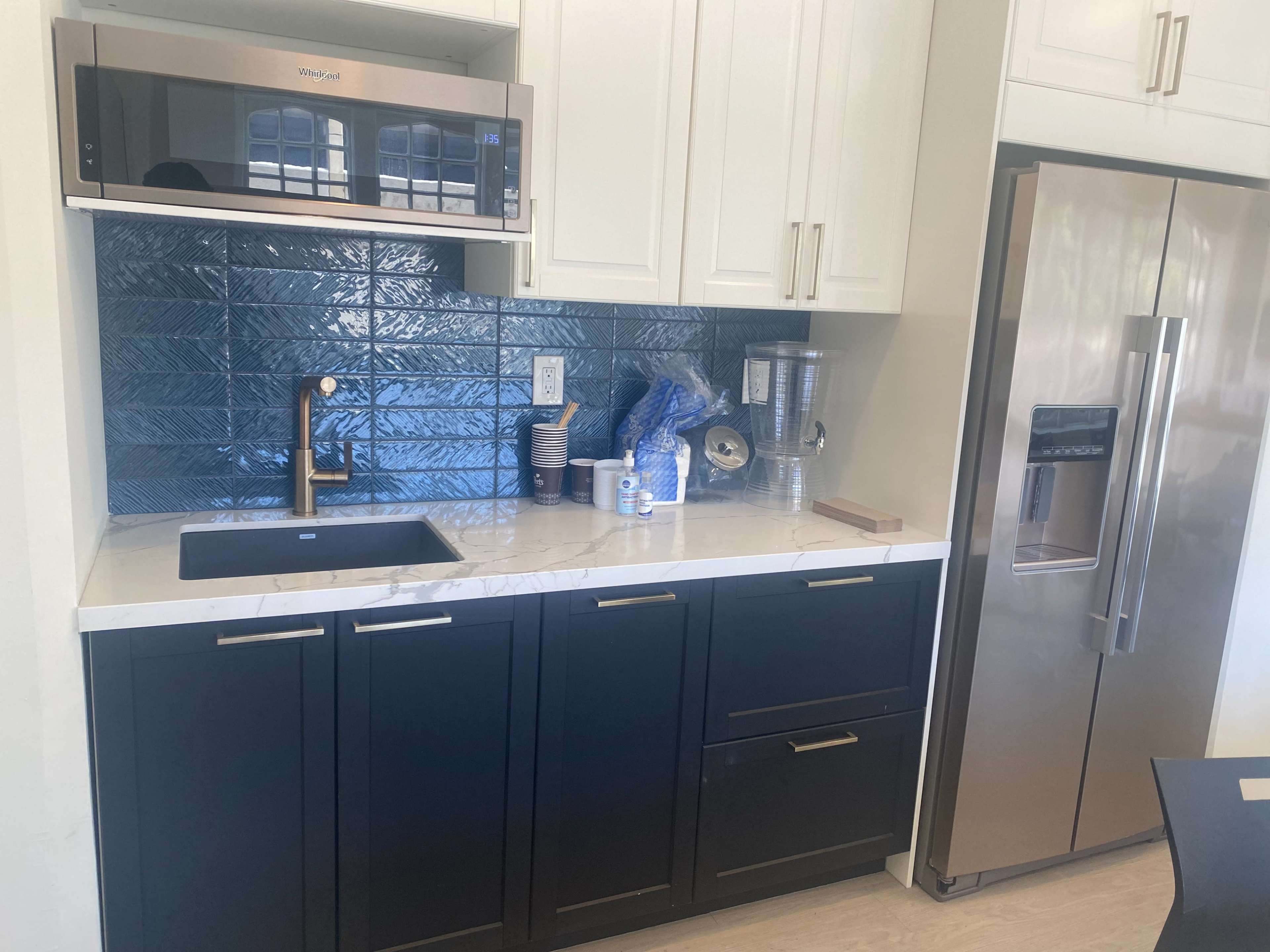 A modern kitchen with dark cabinetry, a stainless steel refrigerator, a microwave above the sink, and a blue tiled backsplash.